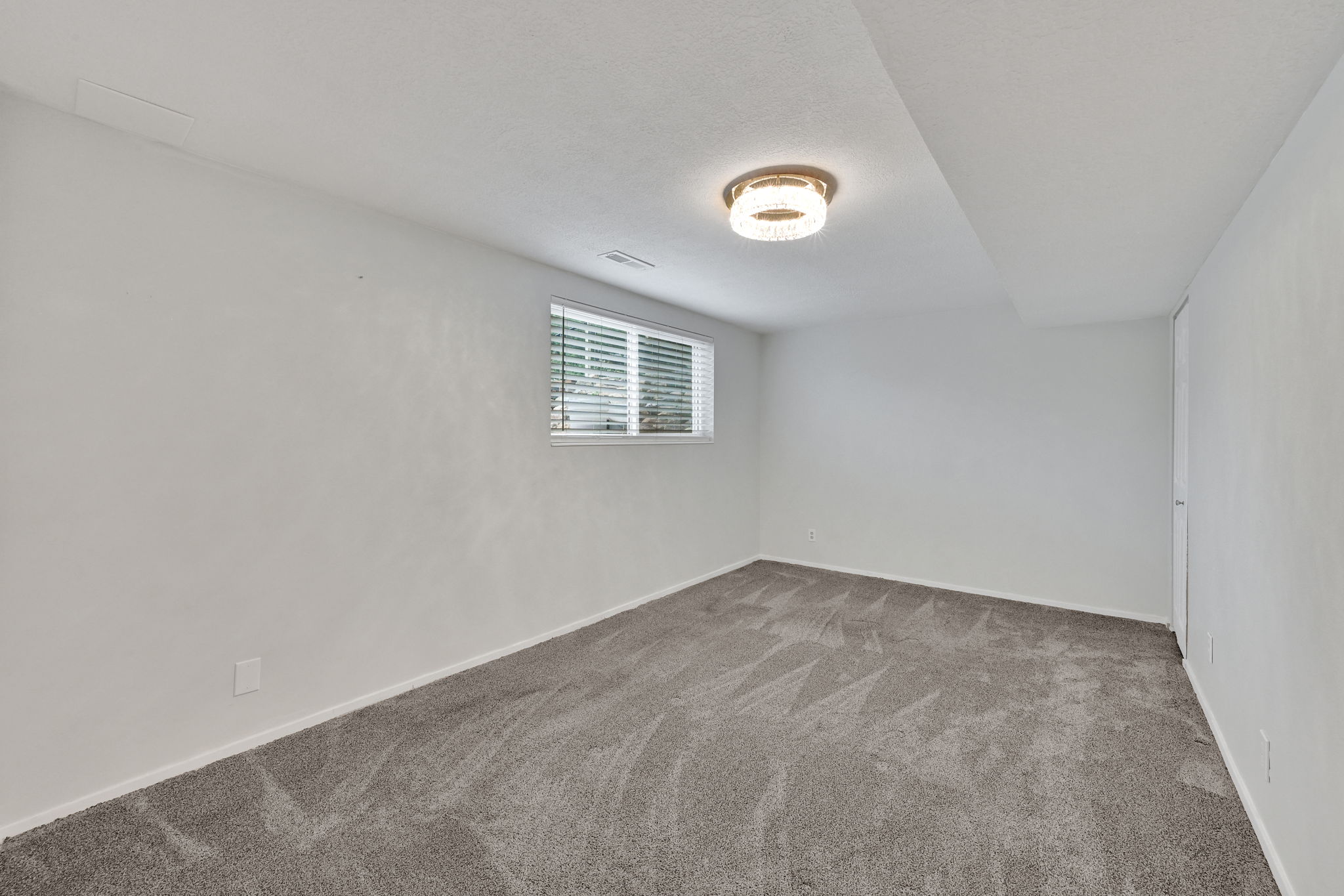 Carpeted interior space featuring a window with horizontal blinds, a flush-mount ceiling light fixture, and white wall finishes