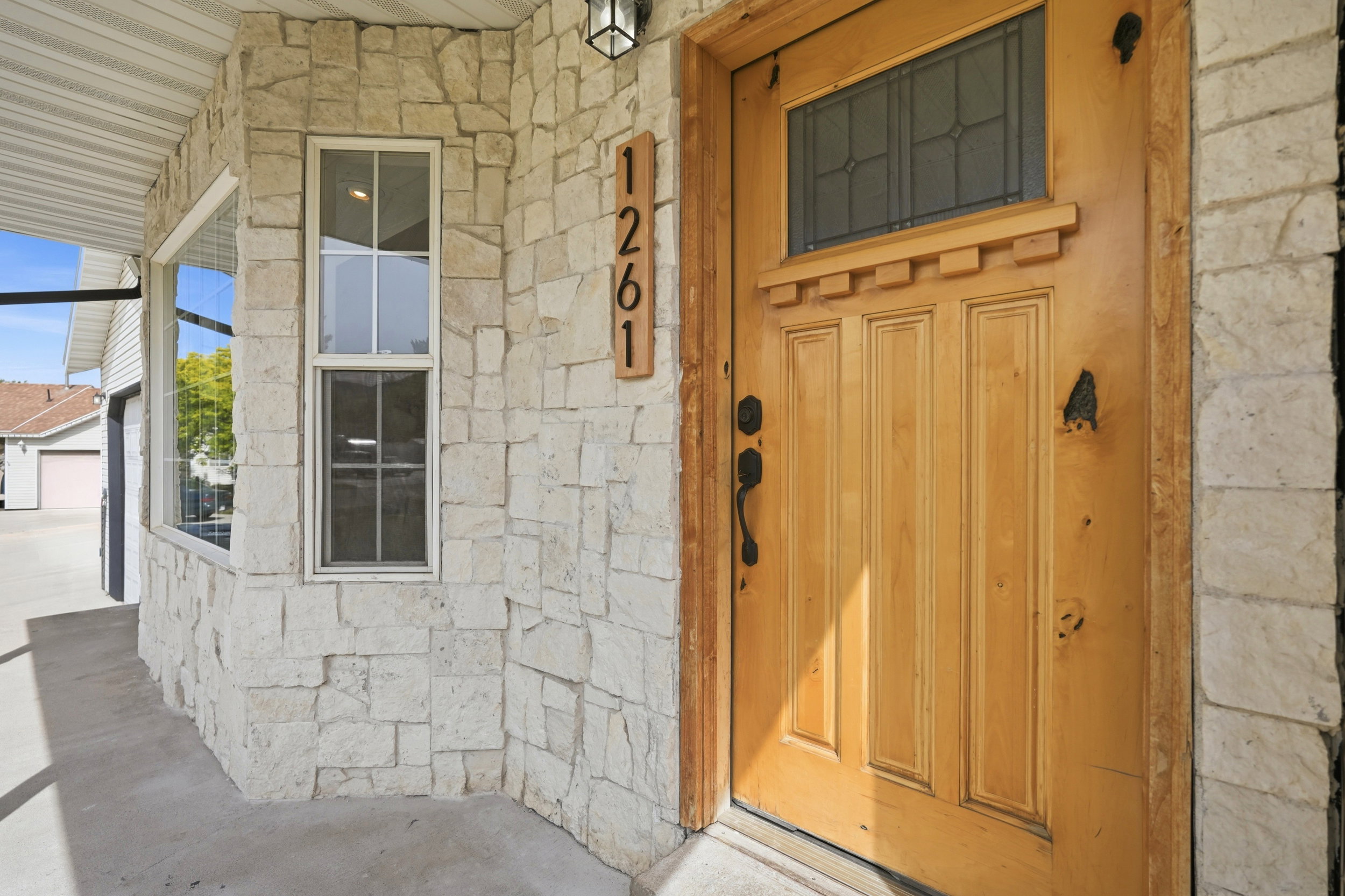 Stone veneer exterior featuring a paneled wood-finish door with decorative glass, a porch light fixture, and a vertical house number plaque