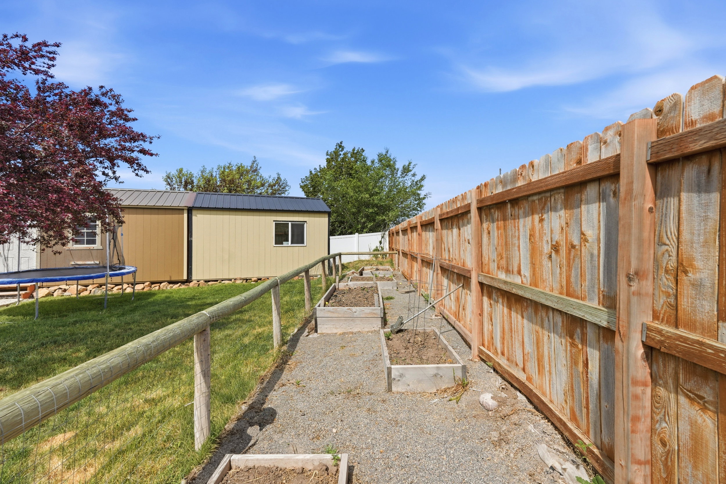 Backyard area featuring raised garden beds with a gravel pathway, a wood privacy fence, and a perimeter wire fence