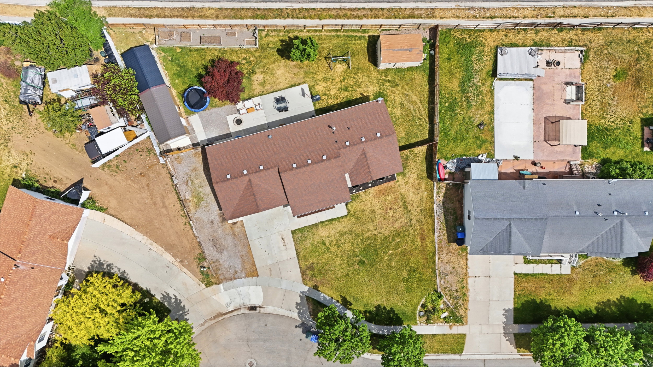 Aerial overview showcasing a property with a brown-roofed residence, extensive paved areas, and surrounding green spaces