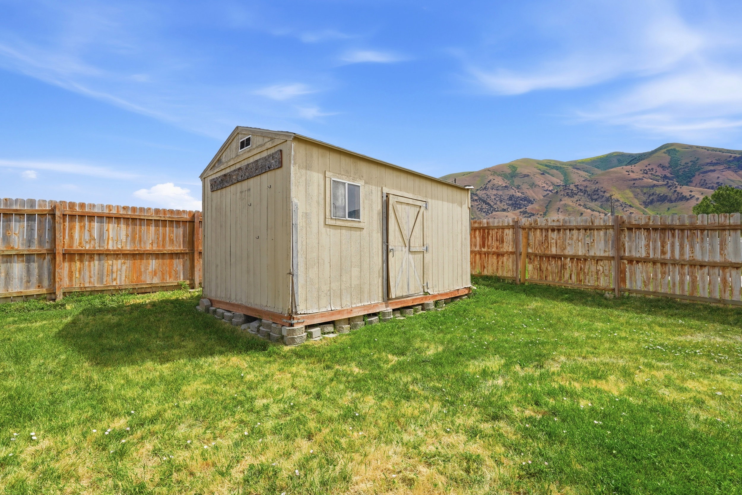 Detached storage shed with a single window, double doors, and a wood-slat privacy fence