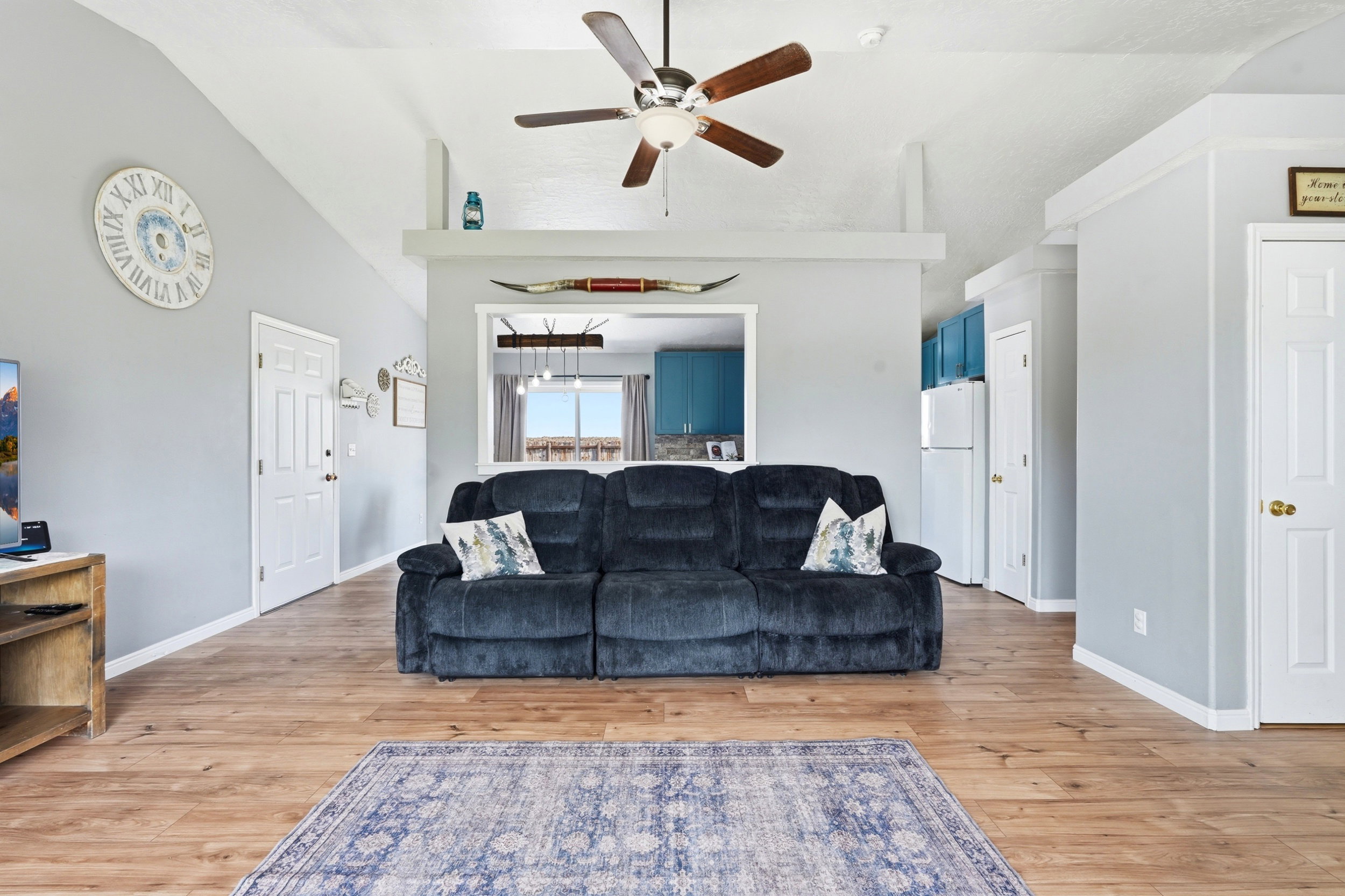 Living area featuring a vaulted ceiling with a ceiling fan, wood-finish flooring, and white trim
