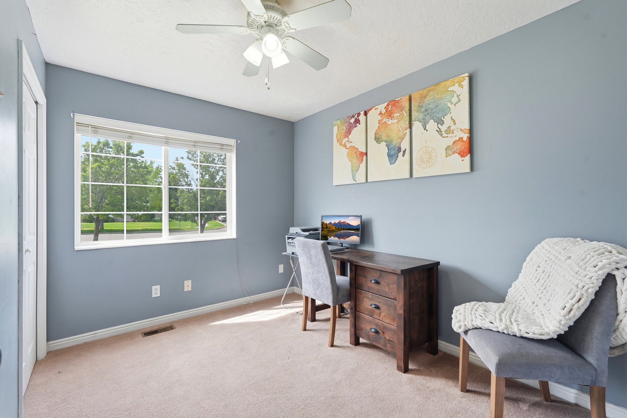 Spacious room featuring a large window overlooking mature trees, light blue walls, and neutral carpeting