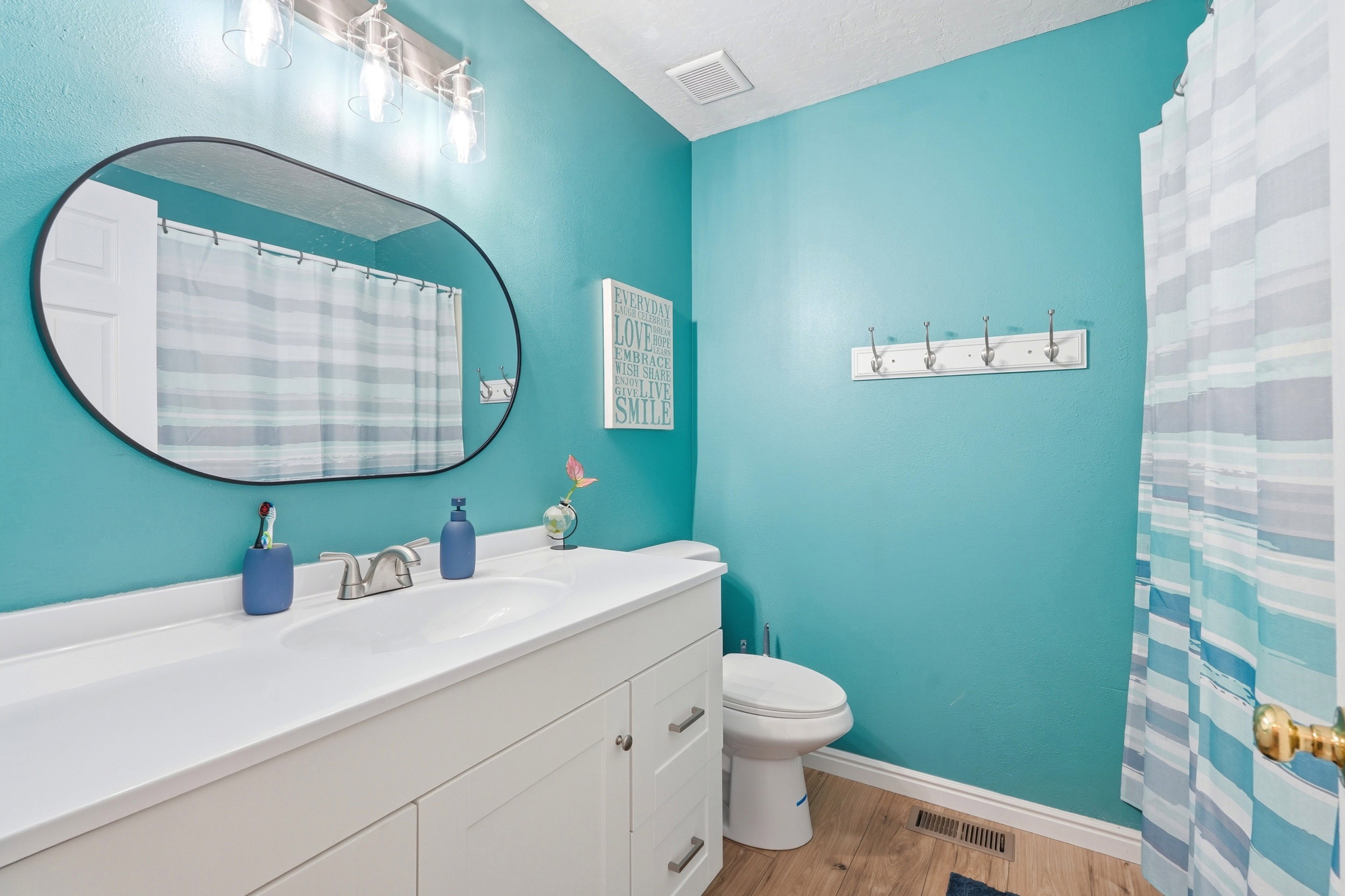 Bathroom featuring a single vanity with an integrated sink and white cabinetry, brushed nickel faucet, an oval mirror, and wood-finish flooring