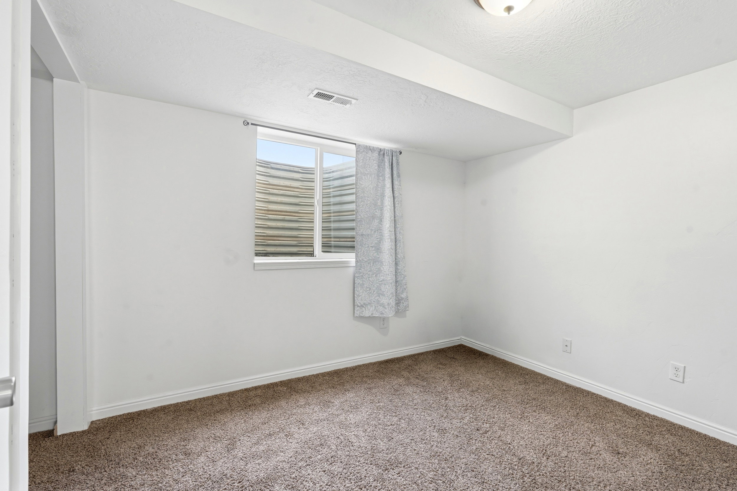 Carpeted room with white walls, a single window, and a flush-mount ceiling light fixture