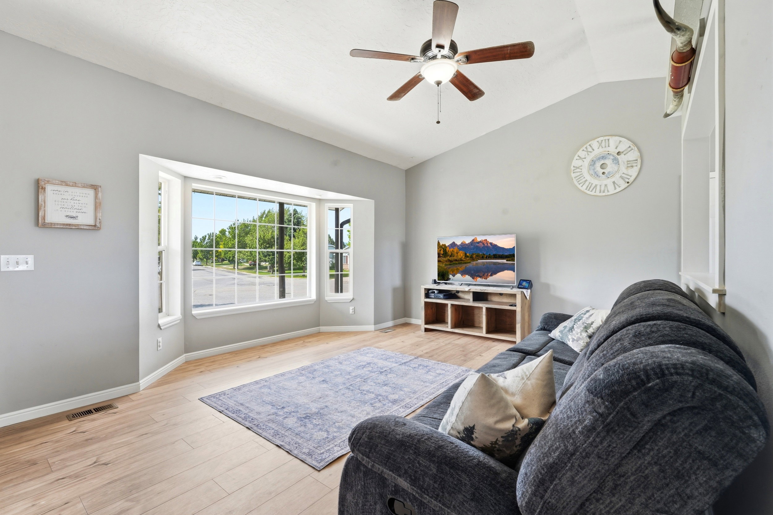 Living area featuring a bay window, vaulted ceiling, wood-finish flooring, and a ceiling fan with integrated lighting