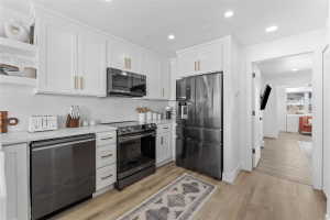 Modern kitchen featuring white shaker cabinetry, stainless steel appliances, white subway tile backsplash, light wood-finish flooring, and recessed lighting