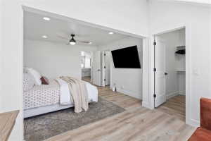 Bedroom featuring recessed lighting and a ceiling fan, wood-finish flooring, a wall-mounted entertainment system, a walk-in closet with built-in shelving, and an en-suite bathroom with a double vanity