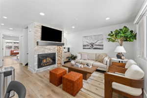 Living area featuring wood-finish flooring, a stone-clad fireplace with a dark wood mantel, a built-in gas firebox, recessed lighting, and a large window