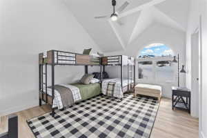Vaulted ceiling room featuring light wood-finish flooring, an arched window with mountain scenery, and a modern ceiling fan