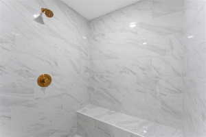Shower enclosure featuring large format white tiled walls with grey veining, a built-in tiled bench, a bronze finish shower head, and a matching bronze finish shower control