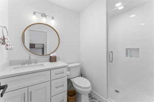 Bathroom featuring a white vanity with integrated sink, a large round mirror, a glass-enclosed shower with subway tile, recessed lighting, and patterned floor tile