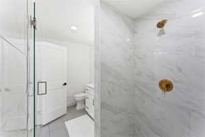 Walk-in shower featuring large format white tiled walls with subtle veining, a glass enclosure, and modern brass fixtures