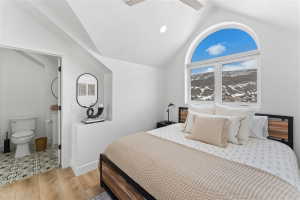Arch-top window with transoms, vaulted ceiling, recessed lighting, wood-finish flooring, and an attached bathroom featuring patterned floor tiles