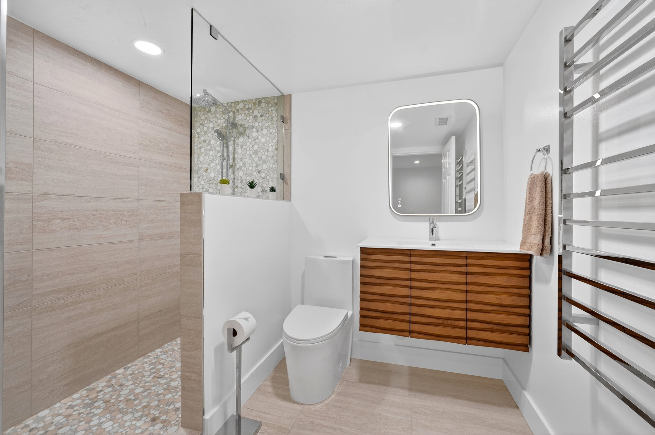 Contemporary bathroom featuring a floating wood-grain vanity with integrated sink, a rectangular illuminated mirror, and a sleek wall-mounted toilet