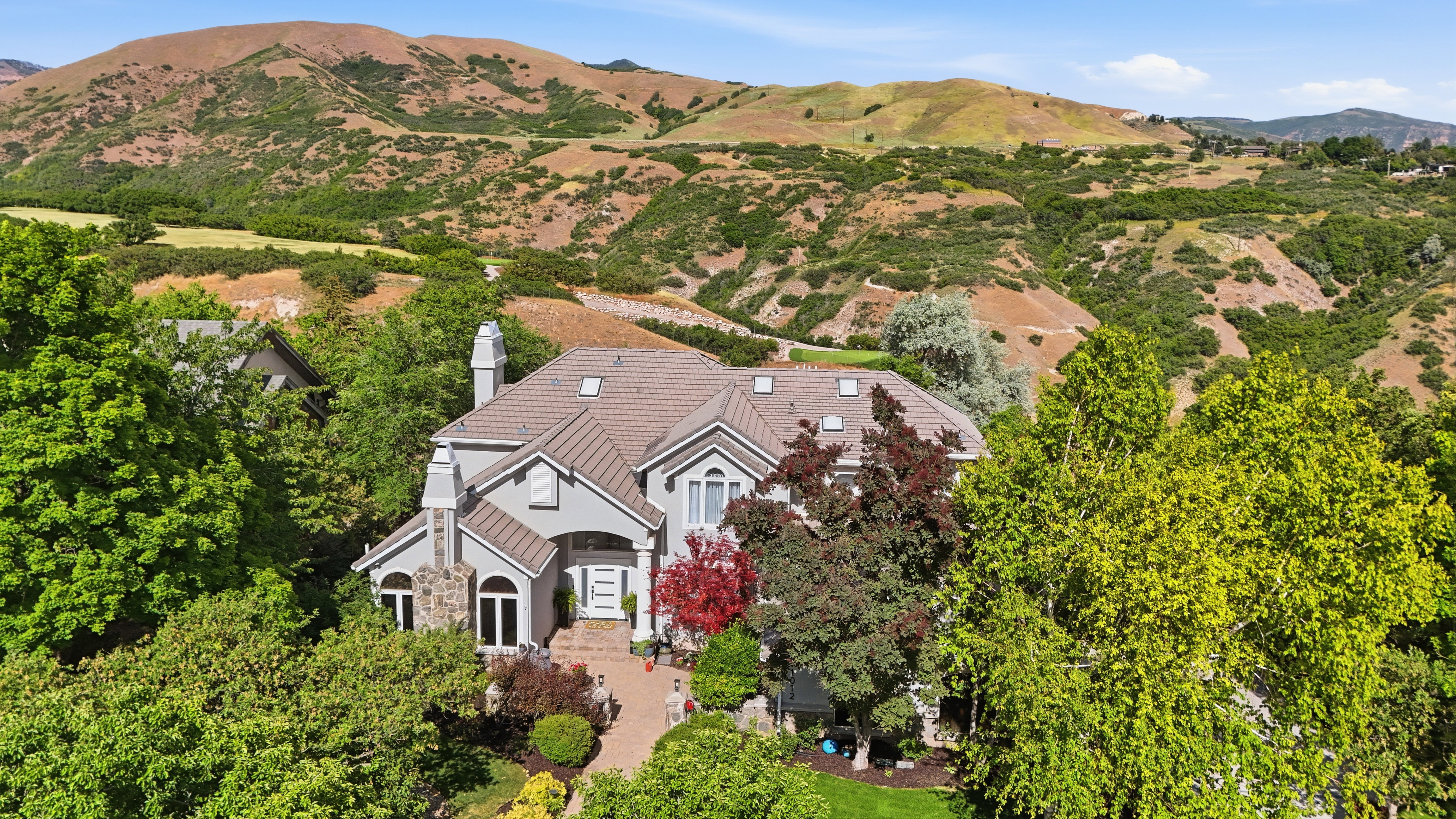Expansive property with a light gray exterior, a multi-gabled roof, and stone-clad chimneys