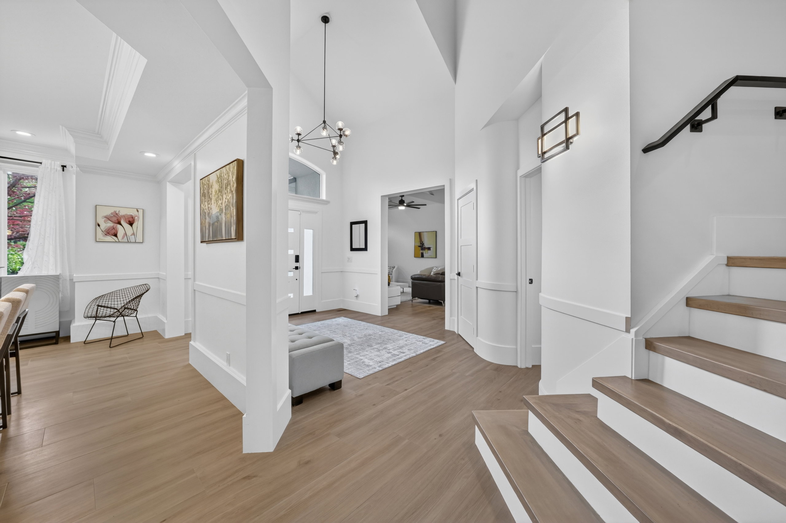 Grand entryway featuring soaring ceilings, wood-finish flooring, a modern chandelier, and a substantial staircase with a black handrail