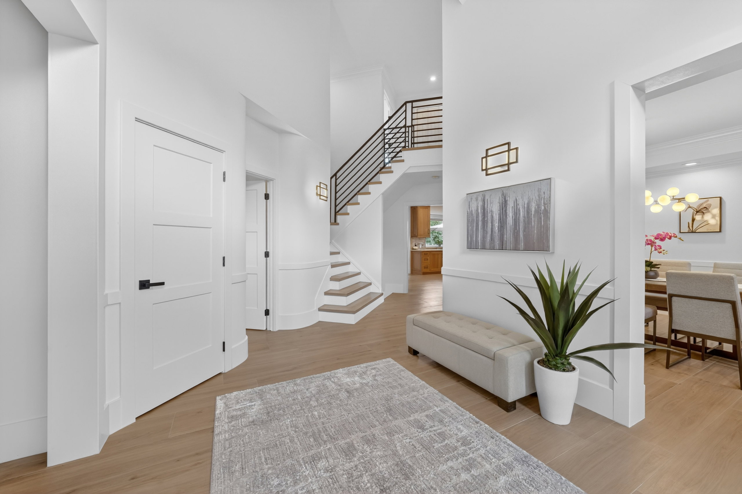 Grand entryway featuring a prominent staircase with black horizontal balusters, light wood-finish flooring, and white paneled walls