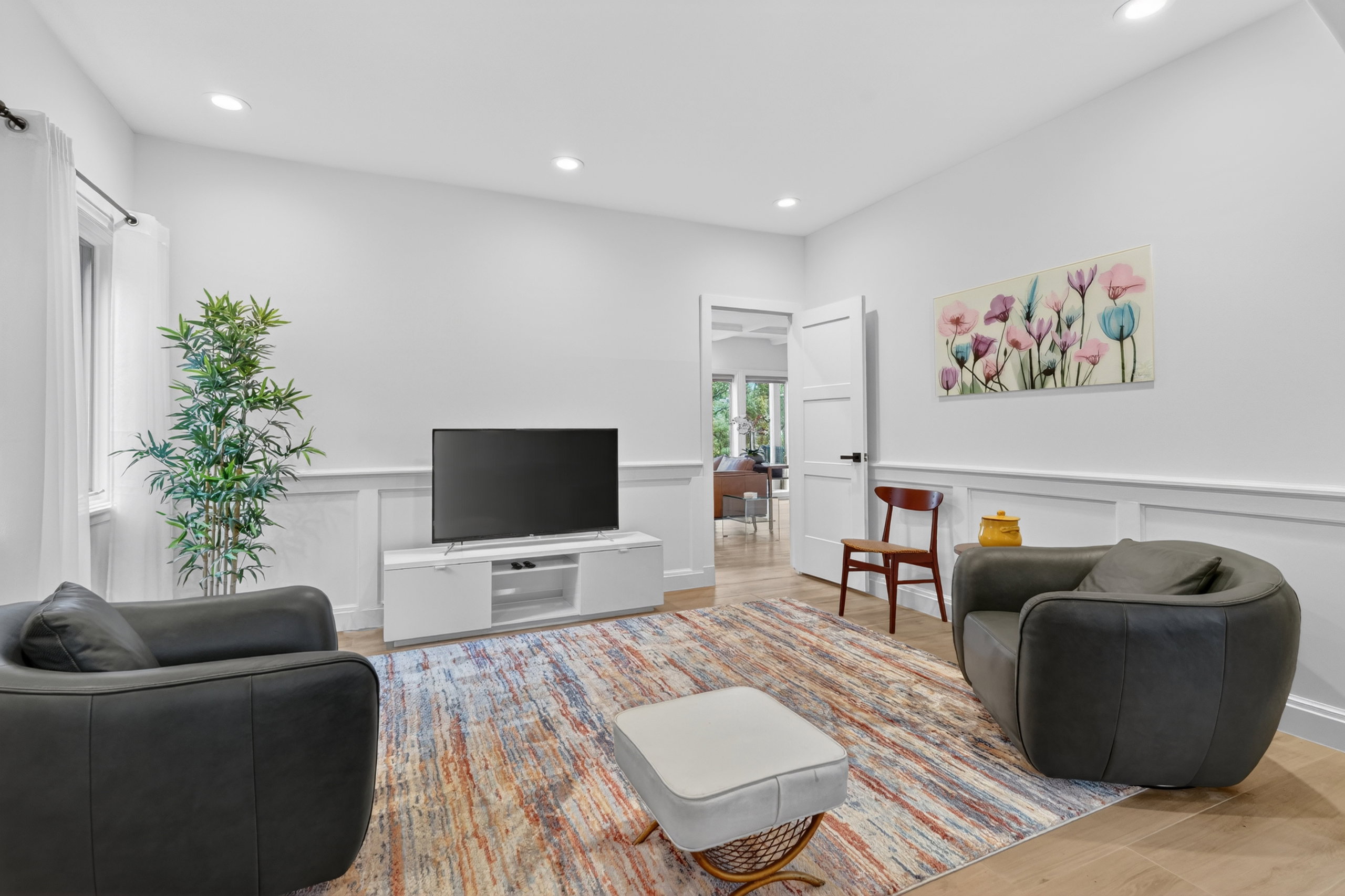 Bright room featuring recessed lighting, light wood-finish flooring, white walls with wainscoting, and a white paneled door