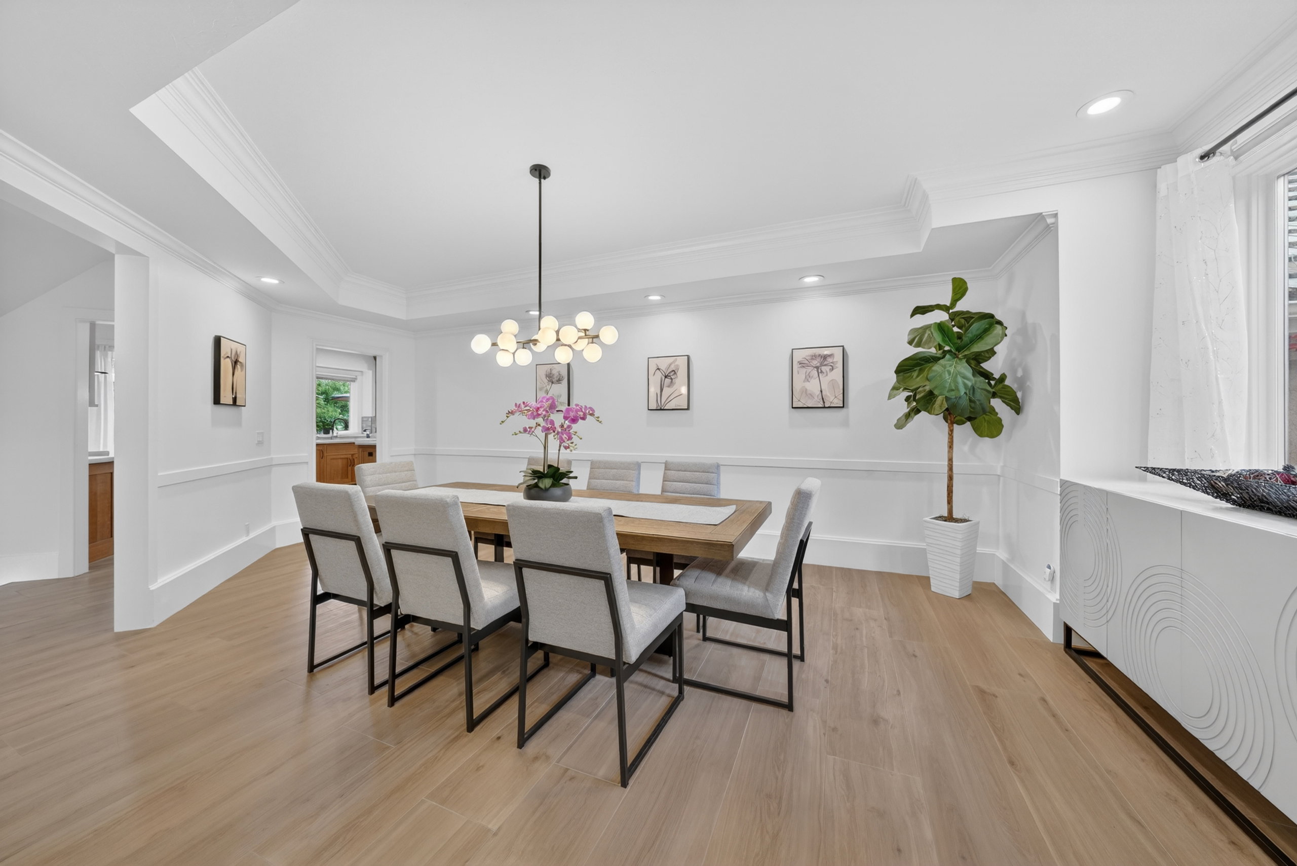 Dining area featuring light wood-finish flooring, white paneled walls, and layered crown molding