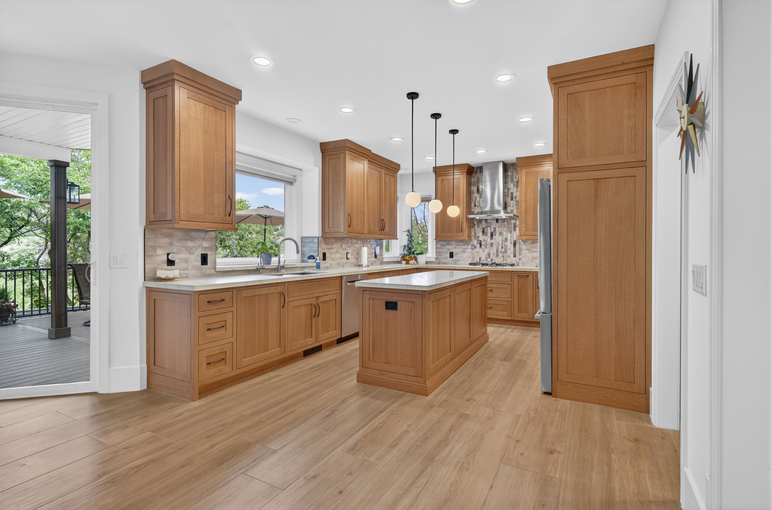 Modern kitchen featuring wood-finish flooring, light wood cabinetry, white countertops, and a tiled backsplash