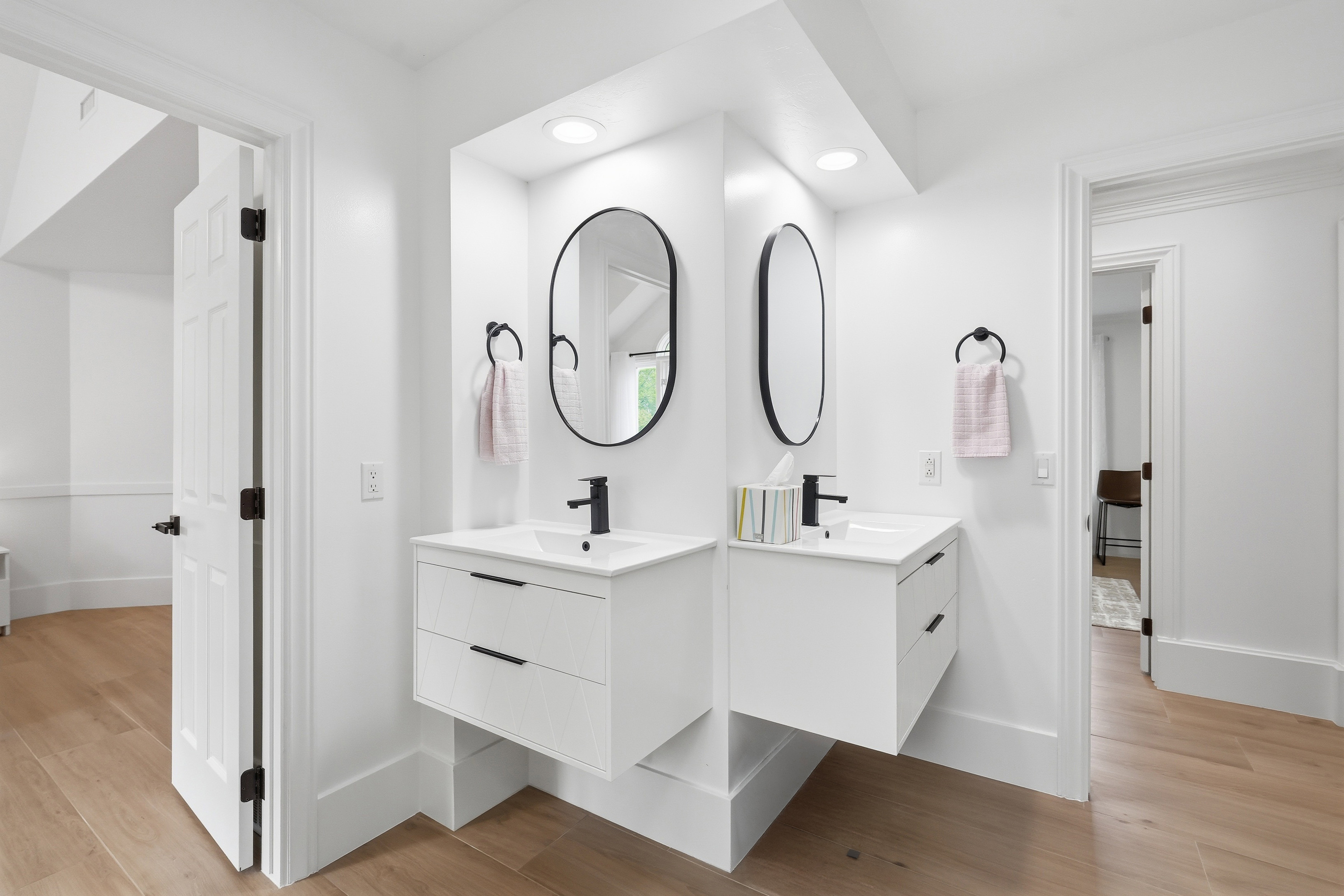 Dual floating vanities featuring white cabinetry, integrated sinks, black fixtures, and oval mirrors