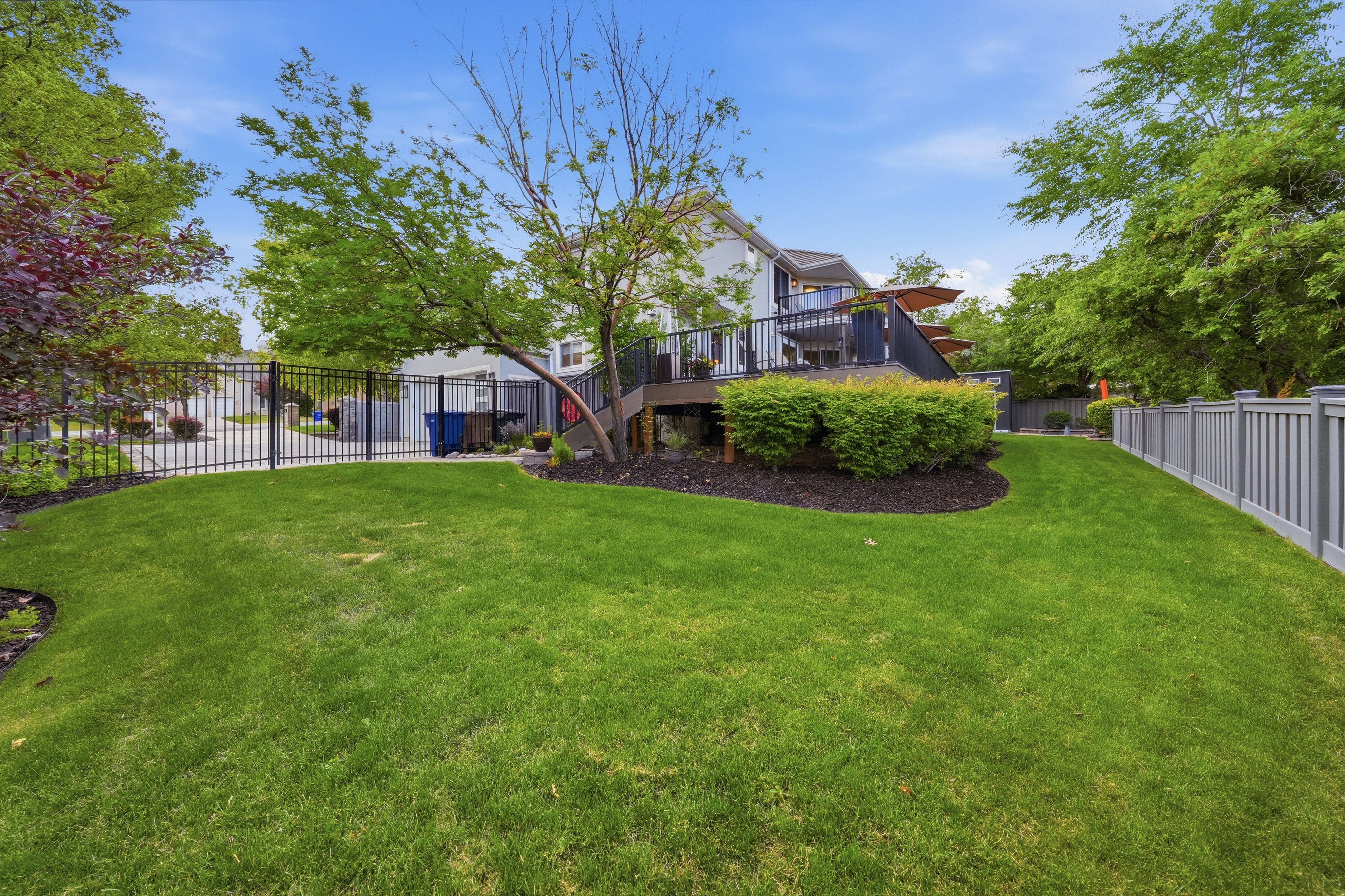 Spacious backyard featuring a large green lawn, mature trees, and a multi-level deck with black railing