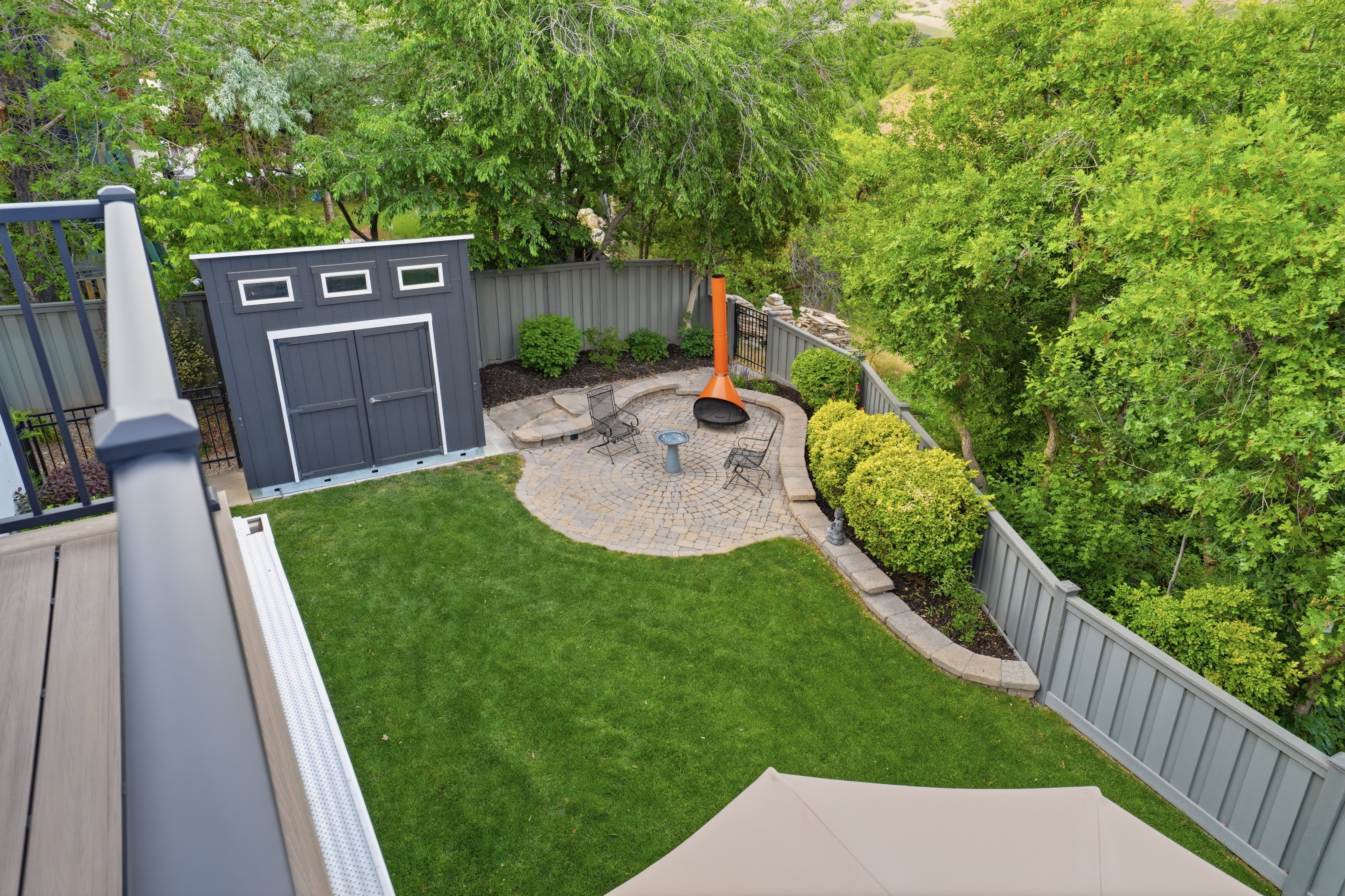 Manicured backyard featuring a paver patio, mature landscaping, a modern storage shed, privacy fencing, and wood-finish decking
