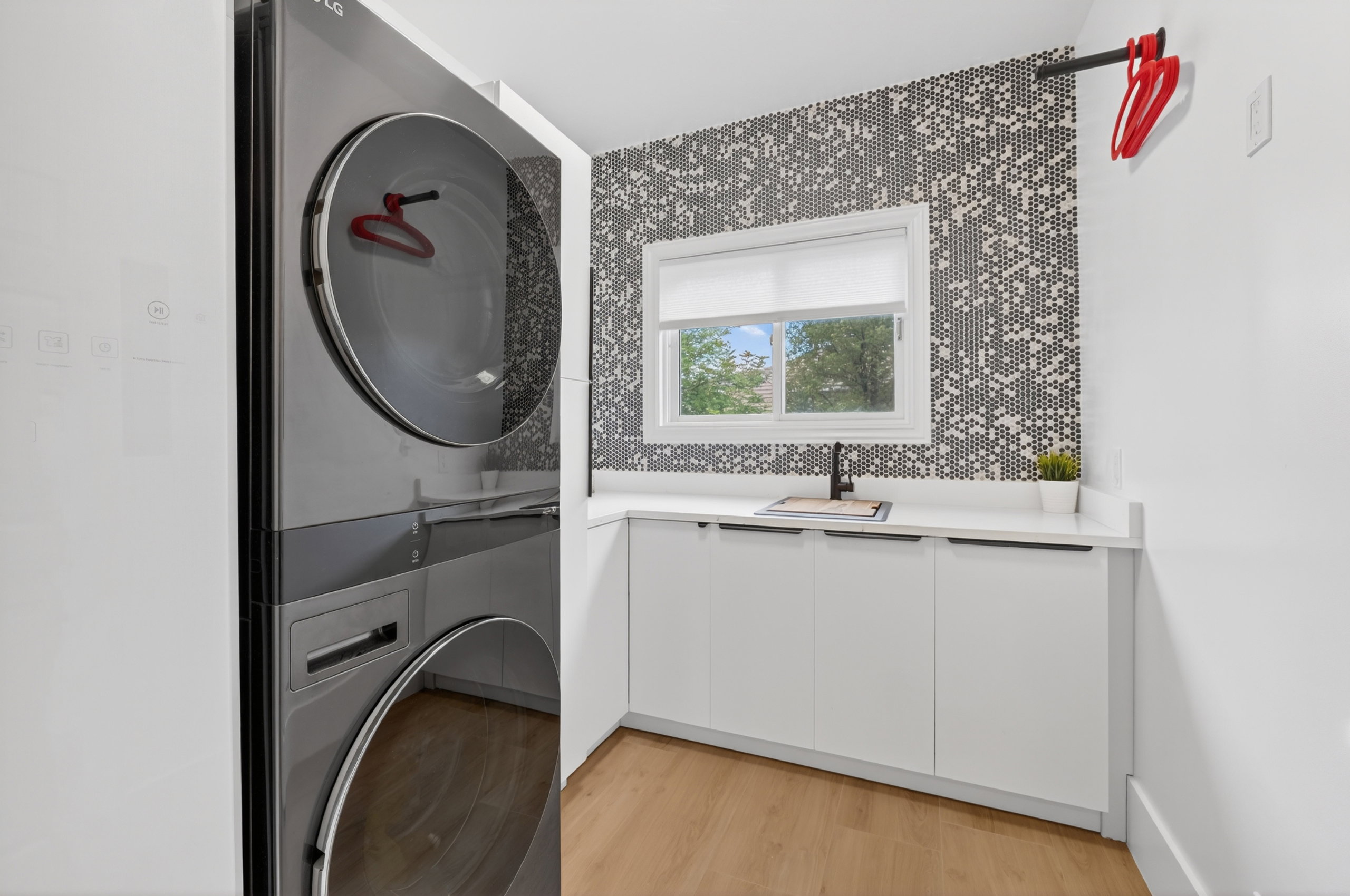 Integrated laundry station featuring stacked appliances, a built-in sink with a matte black faucet, and white cabinetry