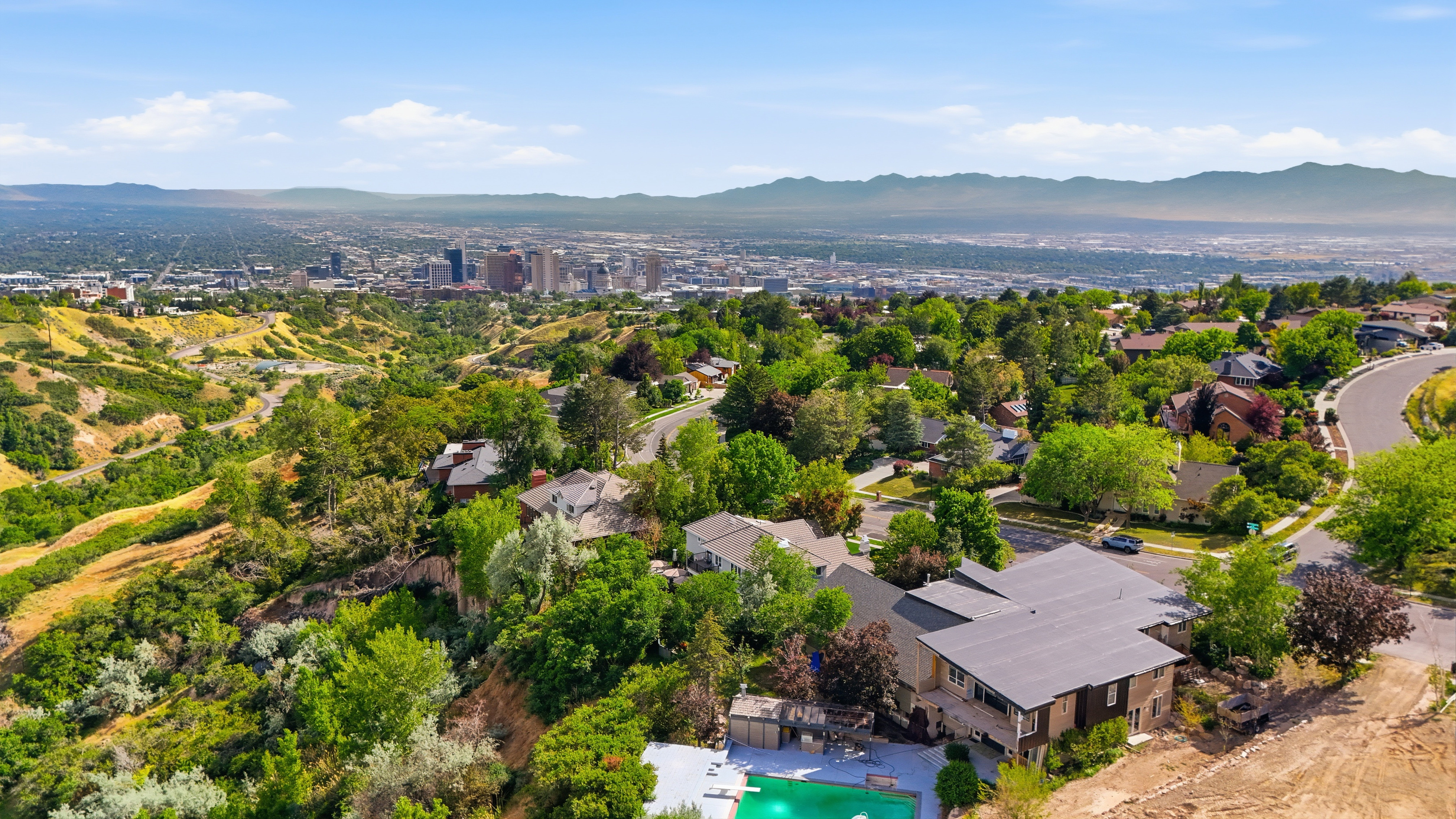 Aerial perspective showcasing a multi-level residence with a dark roof and a concrete patio featuring an in-ground pool