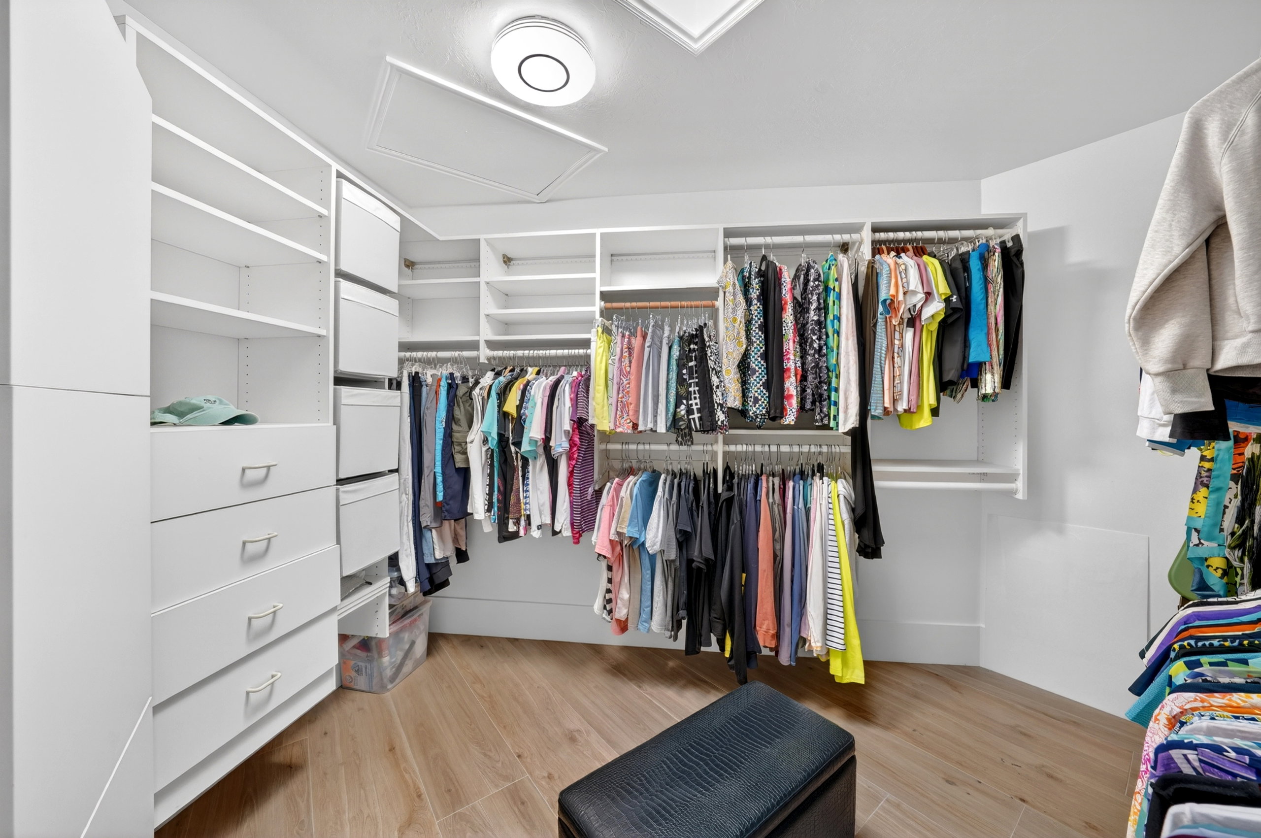 Walk-in closet featuring extensive built-in storage with shelves and drawers, multiple hanging rods, wood-finish flooring, and a flush-mount ceiling light