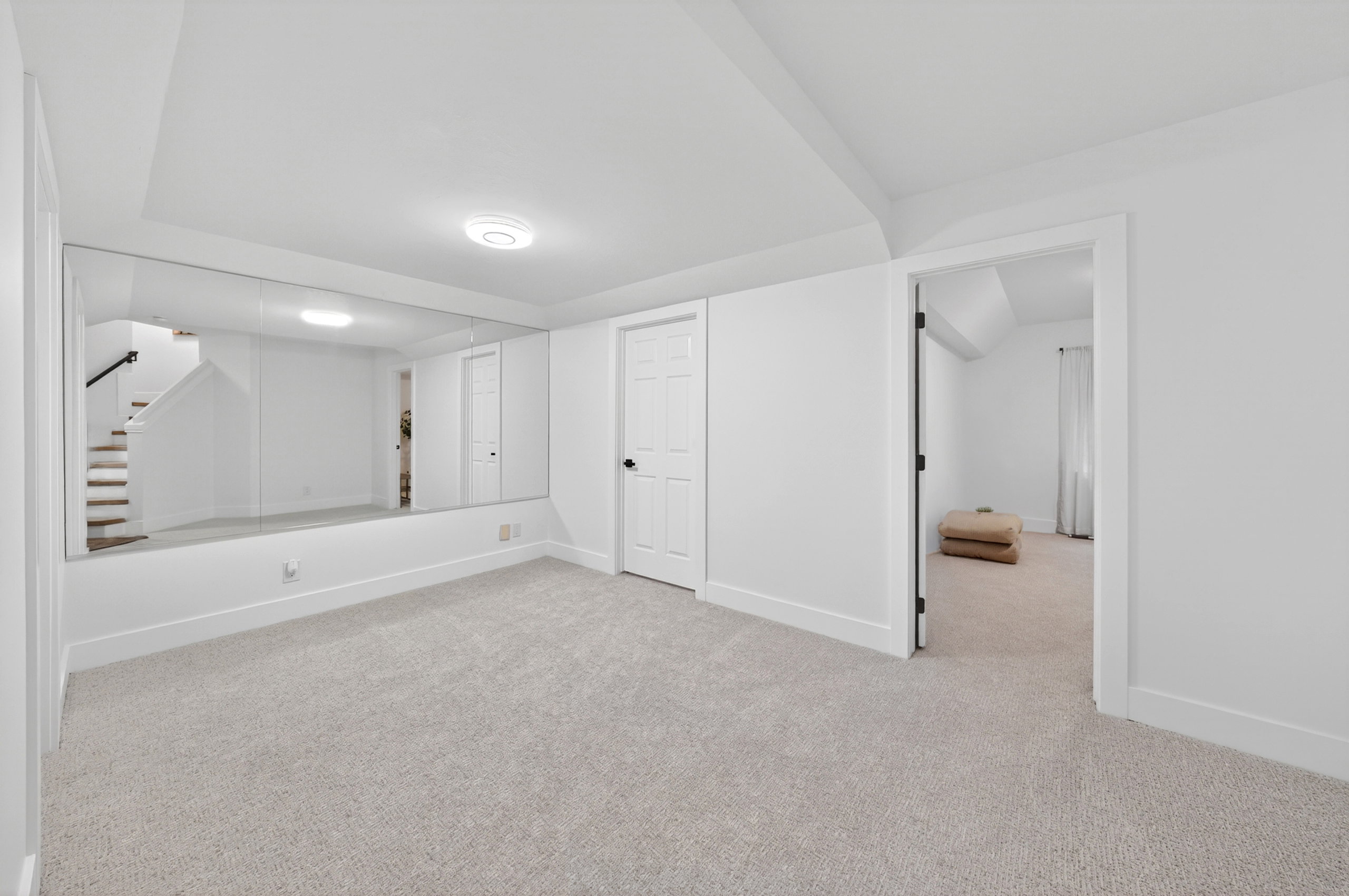 Spacious room featuring a full wall mirror, light-toned carpeting, white walls, and a white paneled door