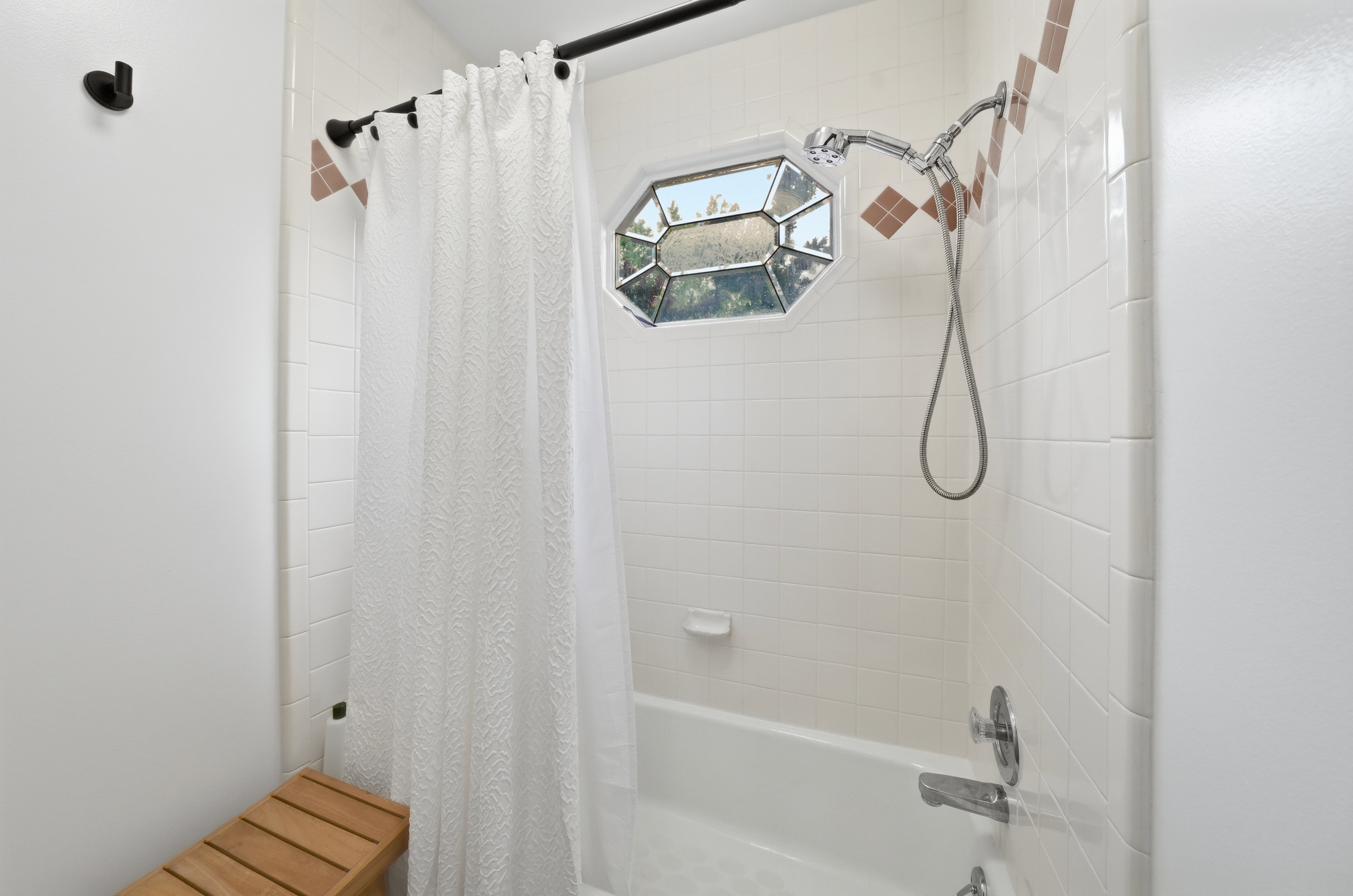 Bathtub with white subway tile surround, accent tile detailing, and an octagonal window