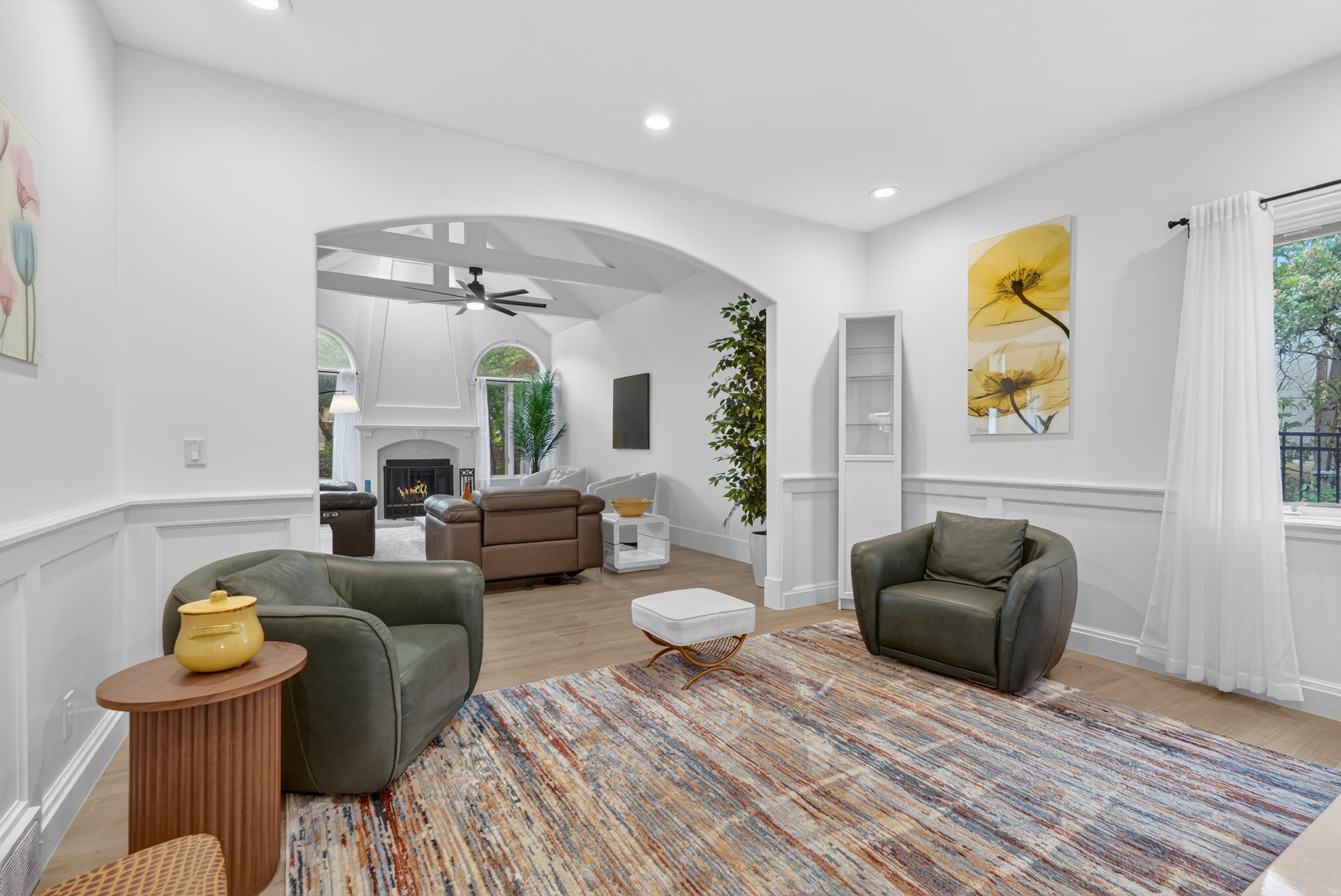 Spacious room featuring wood-finish flooring, wainscoting, and an arched doorway leading to a further living area with a vaulted ceiling and fireplace