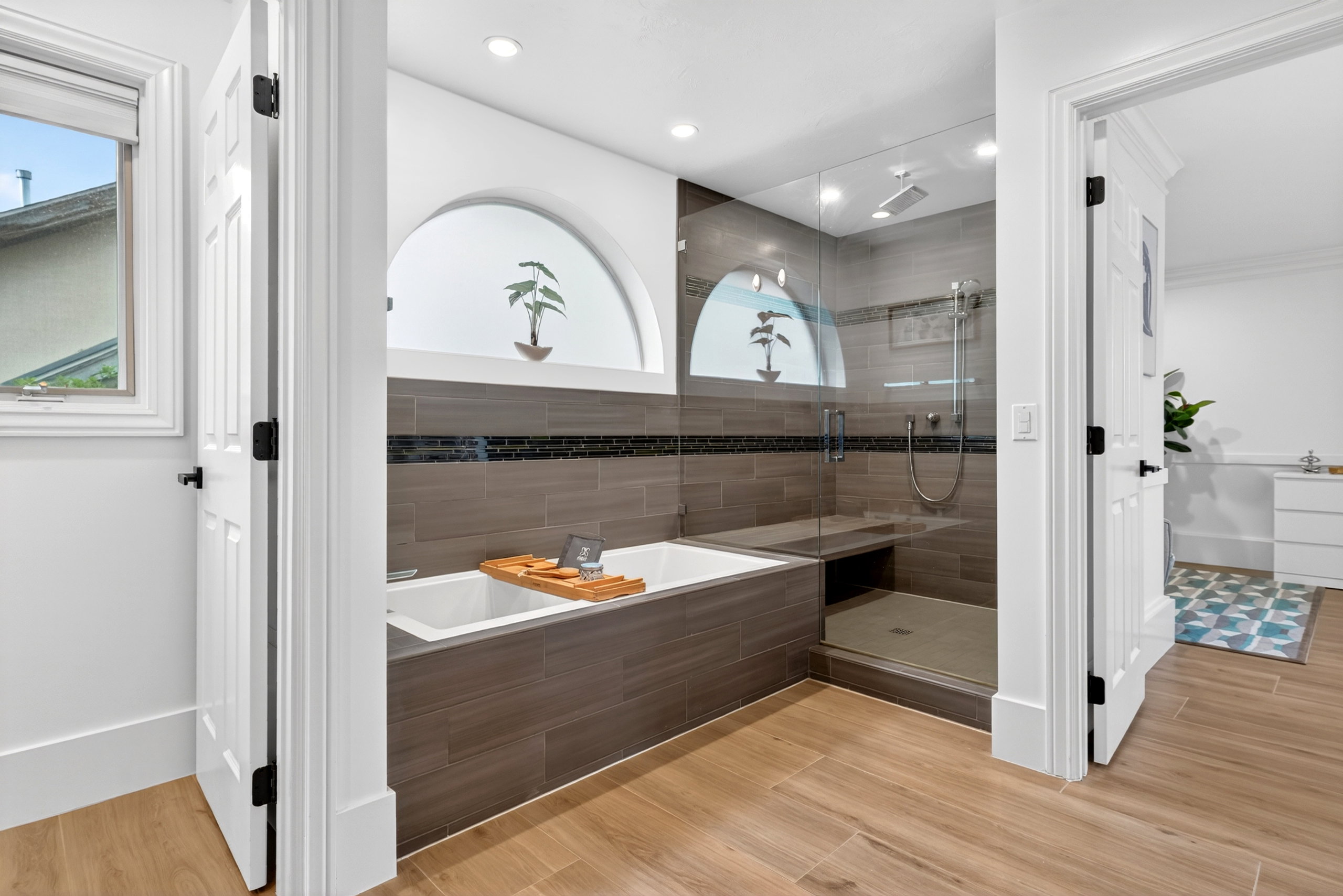 Bathroom featuring a built-in soaking tub, a glass-enclosed shower with a bench, and wood-finish flooring