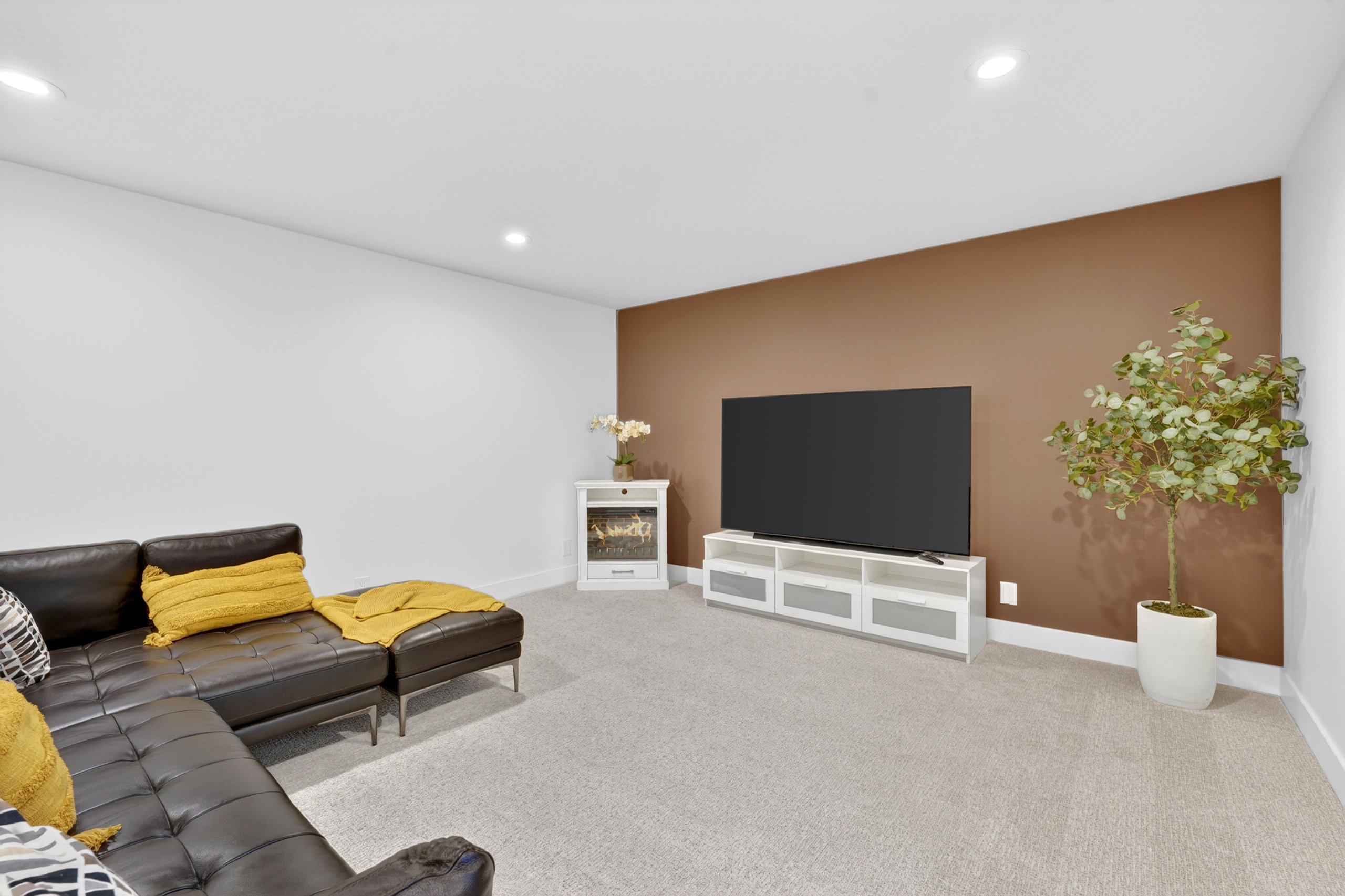 Spacious room with plush carpet flooring, recessed lighting, white baseboards, and a feature wall in a warm brown tone
