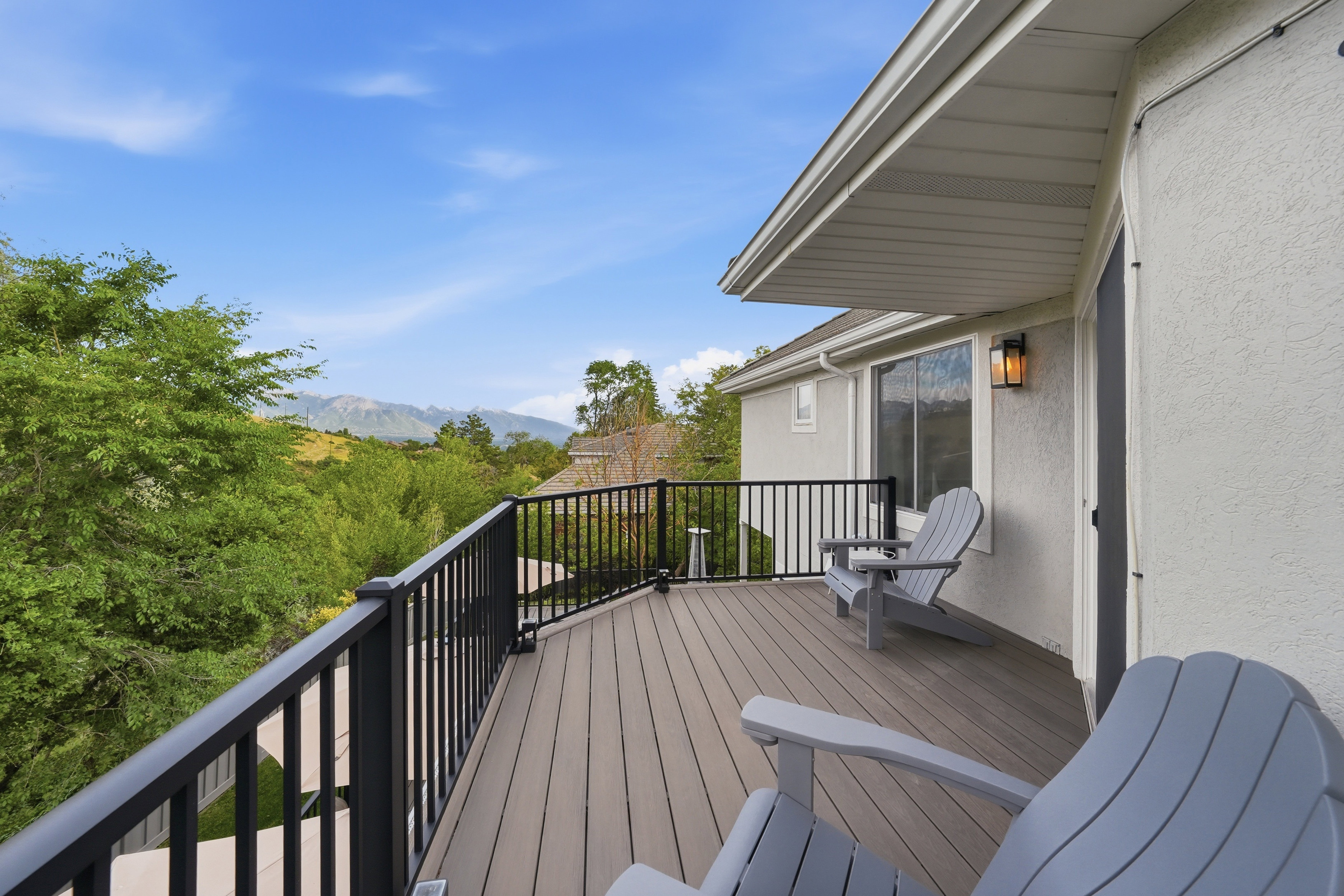 Spacious outdoor deck featuring composite wood-finish flooring, black metal railings, and a stucco exterior