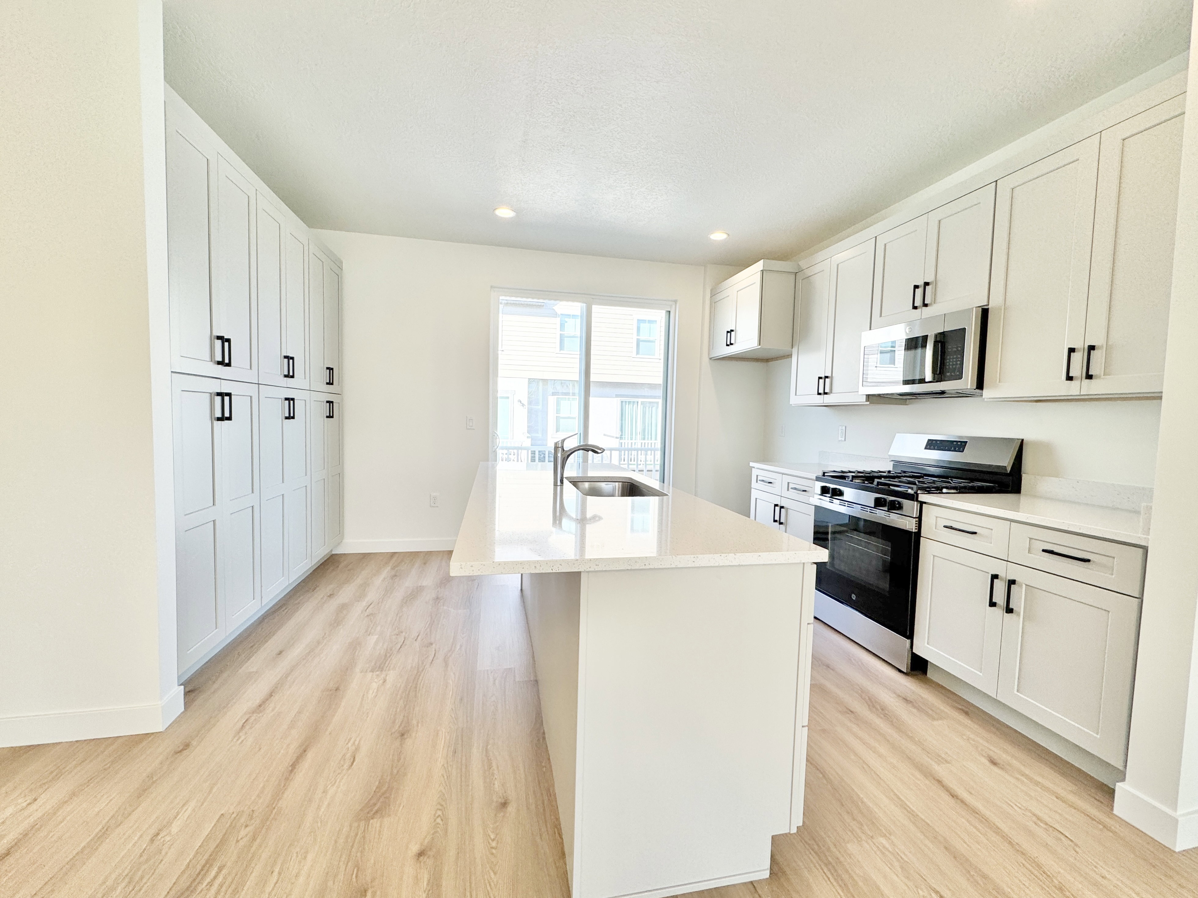 Kitchen featuring an oversized center island, light wood-finish flooring, white shaker-style cabinetry, stainless steel appliances, and a full wall of pantry storage