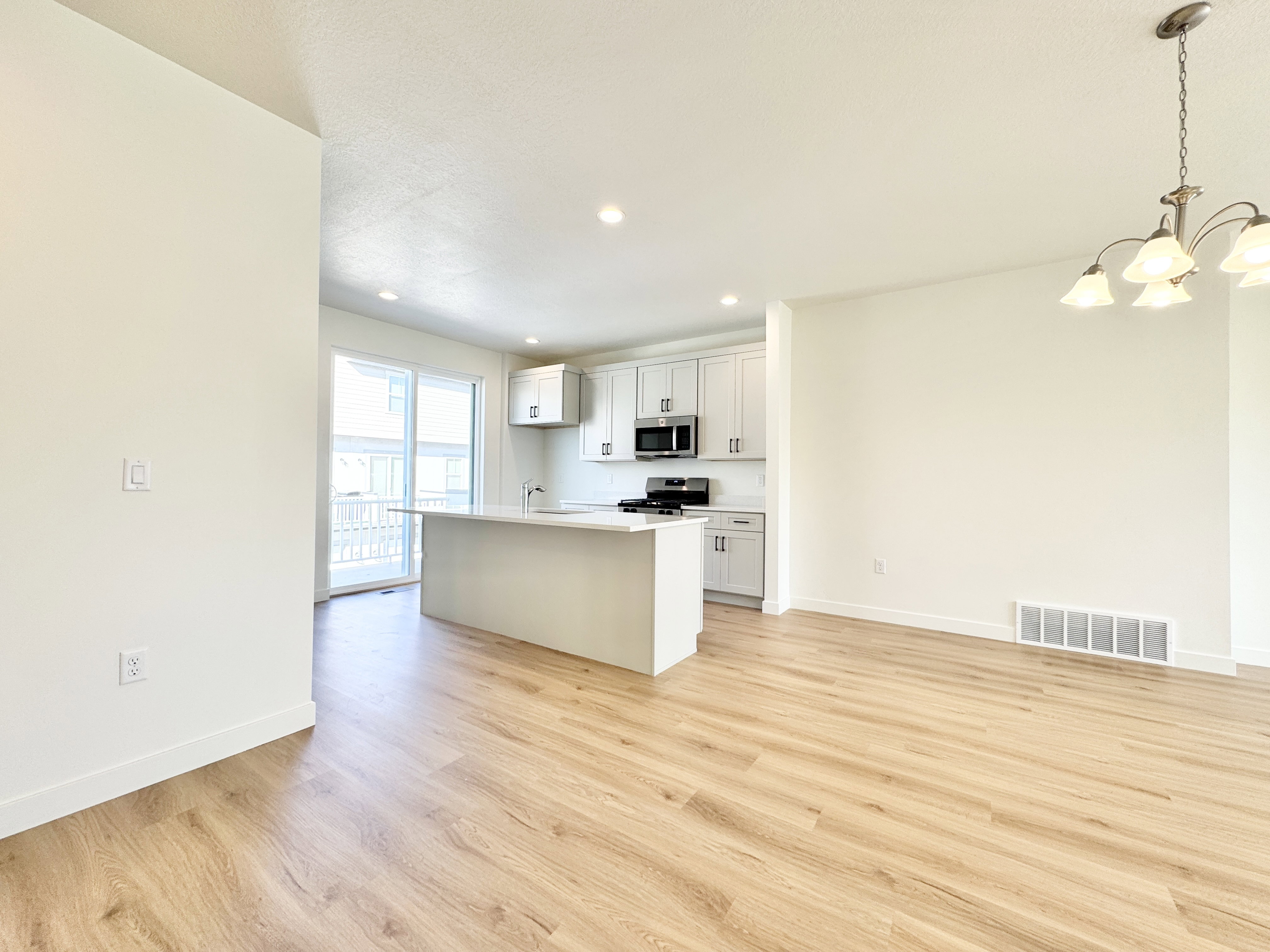 Open-concept living space with wood-finish flooring, a contemporary chandelier, and recessed lighting