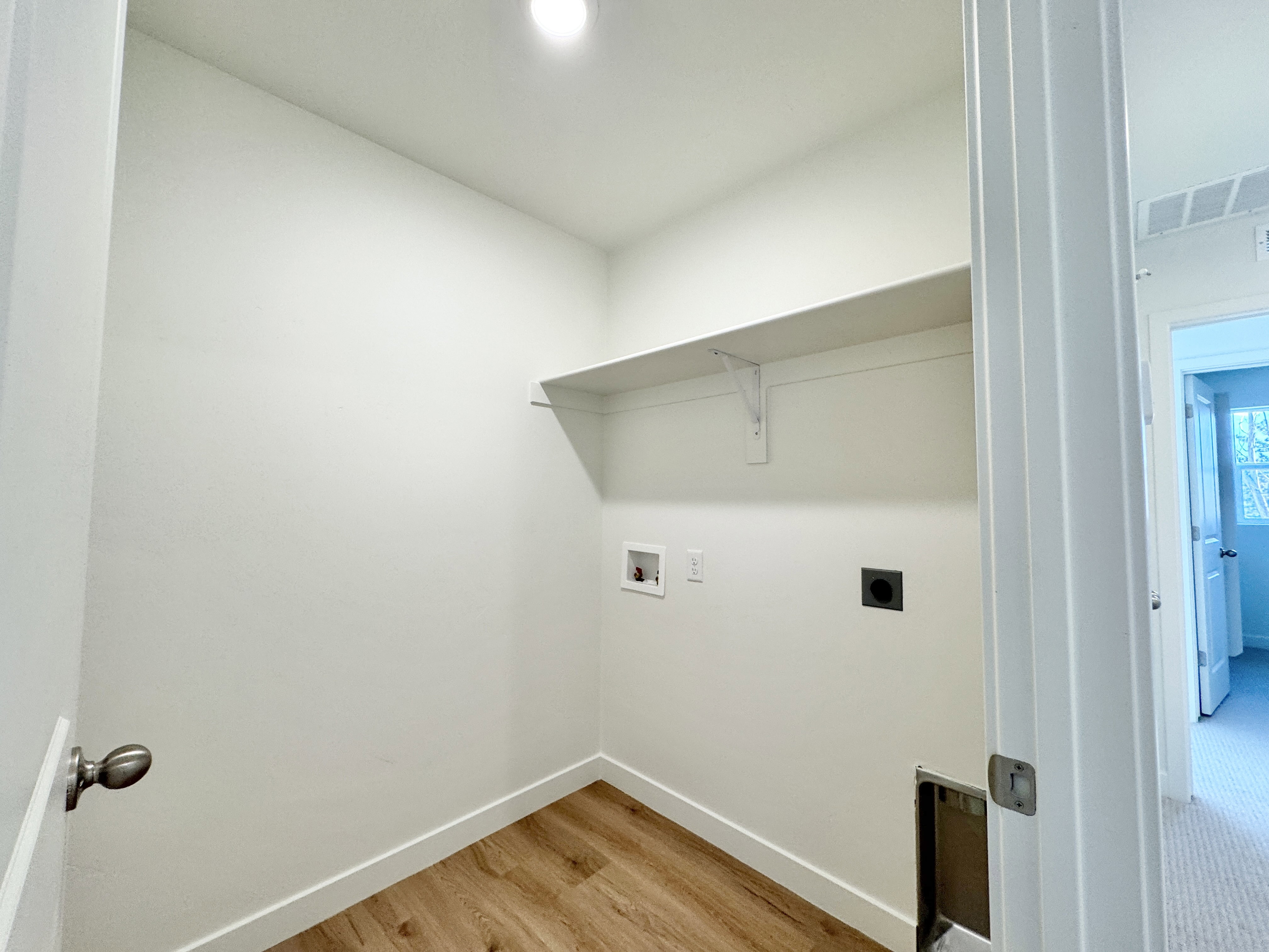 Dedicated laundry area featuring wood-finish flooring, crisp white walls, a built-in wall shelf, and appliance hookups