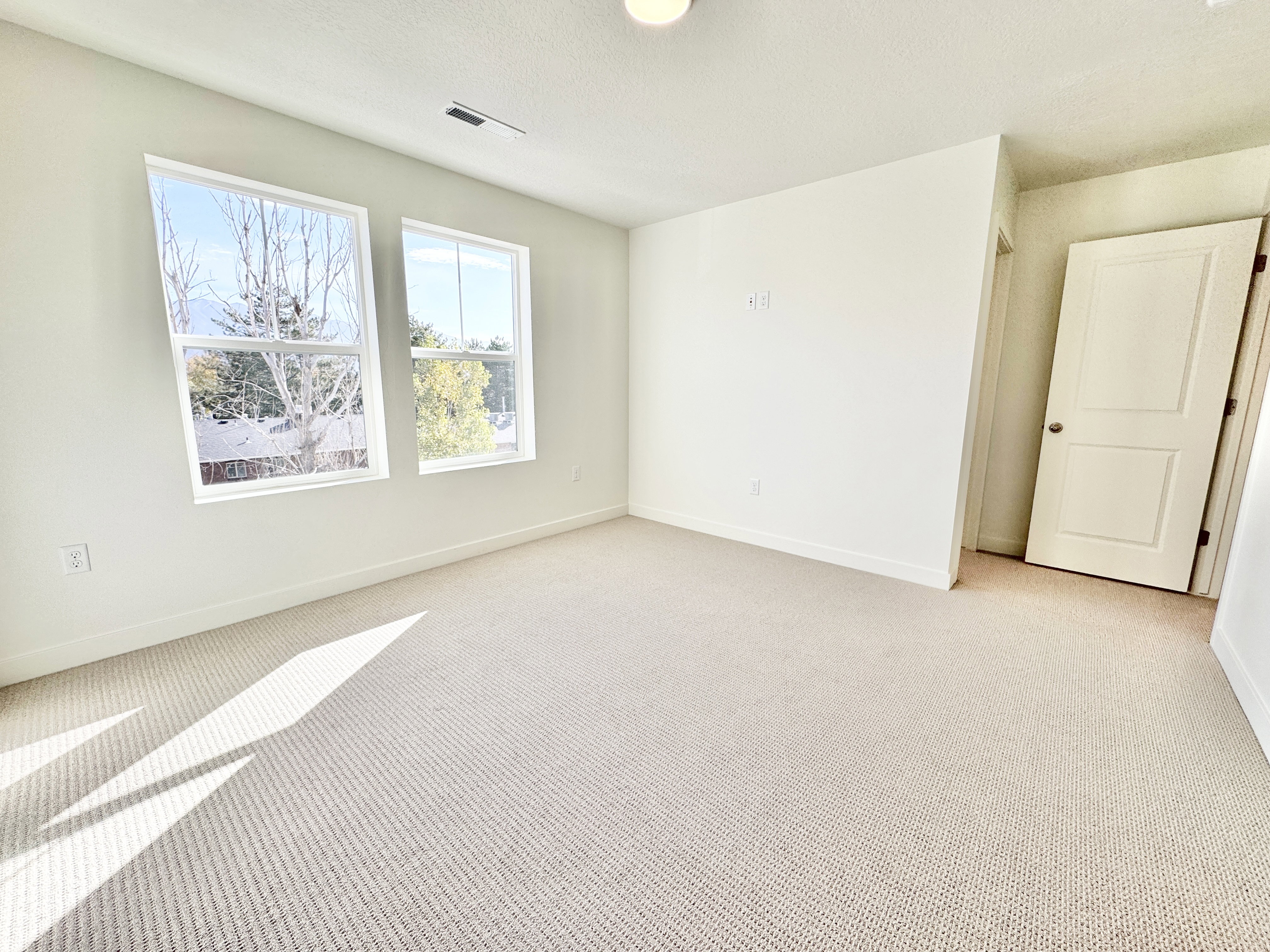 Bright interior space featuring two large windows, neutral-toned wall paint, and light-colored carpet flooring