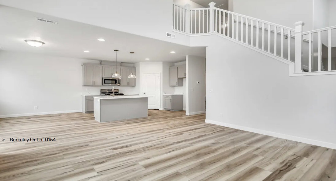 Open-concept living area featuring light wood-finish flooring, a kitchen island with pendant lighting, light gray cabinetry, and a prominent staircase with white railings