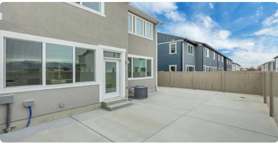 Spacious concrete patio with access to the interior through a glass-paneled door, bordered by a privacy fence, and featuring large windows with white trim