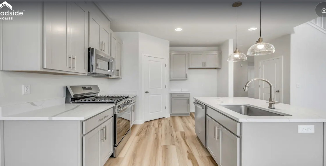 Kitchen featuring light gray cabinetry, stainless steel appliances, a center island with sink, pendant lighting, and wood-finish flooring