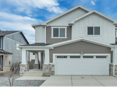 Contemporary facade featuring varied siding textures, a covered entry porch with stone-clad pillars, a two-car garage with transom windows, and white trim accents