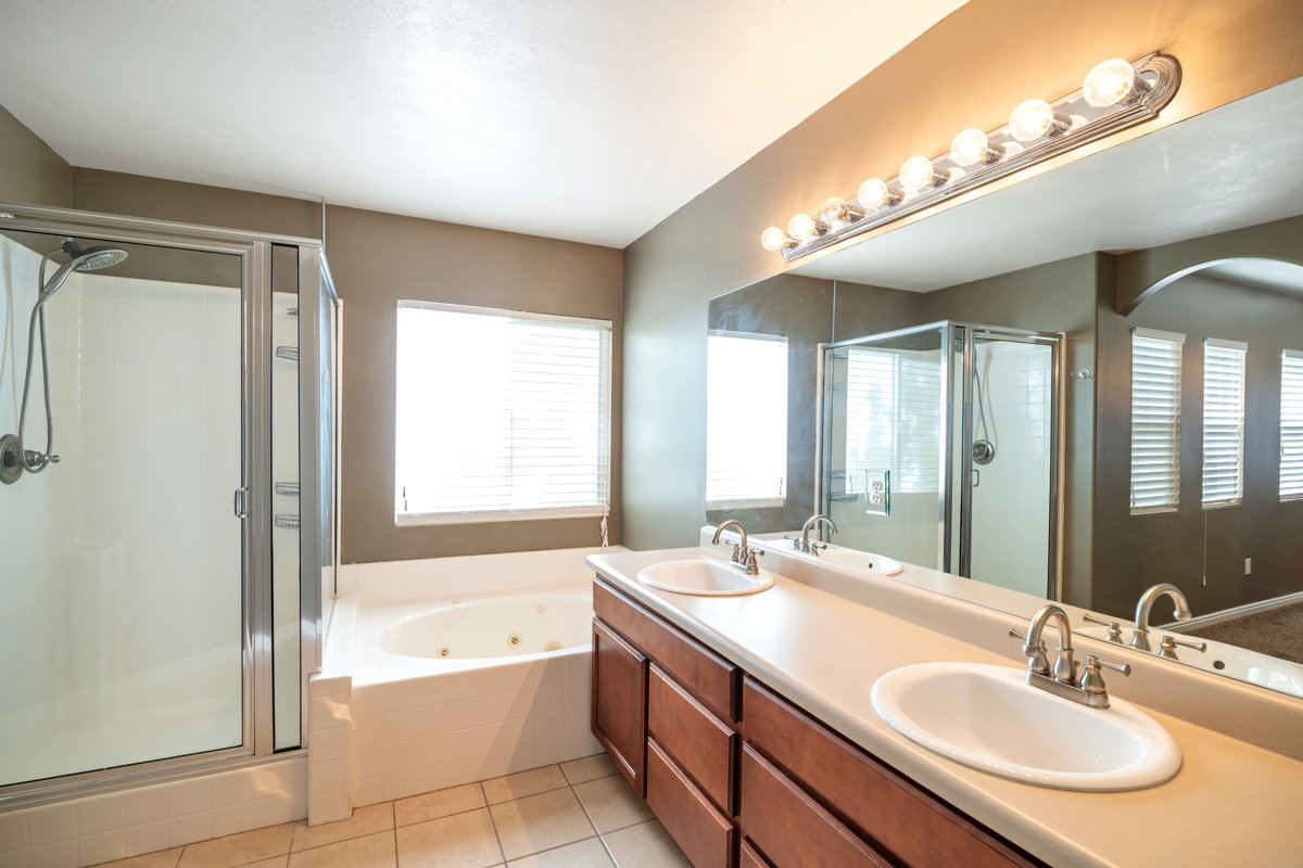 Bathroom featuring a glass-enclosed shower, a jetted soaking tub, a double vanity with a light-toned countertop, wood-finish cabinetry, and tiled flooring
