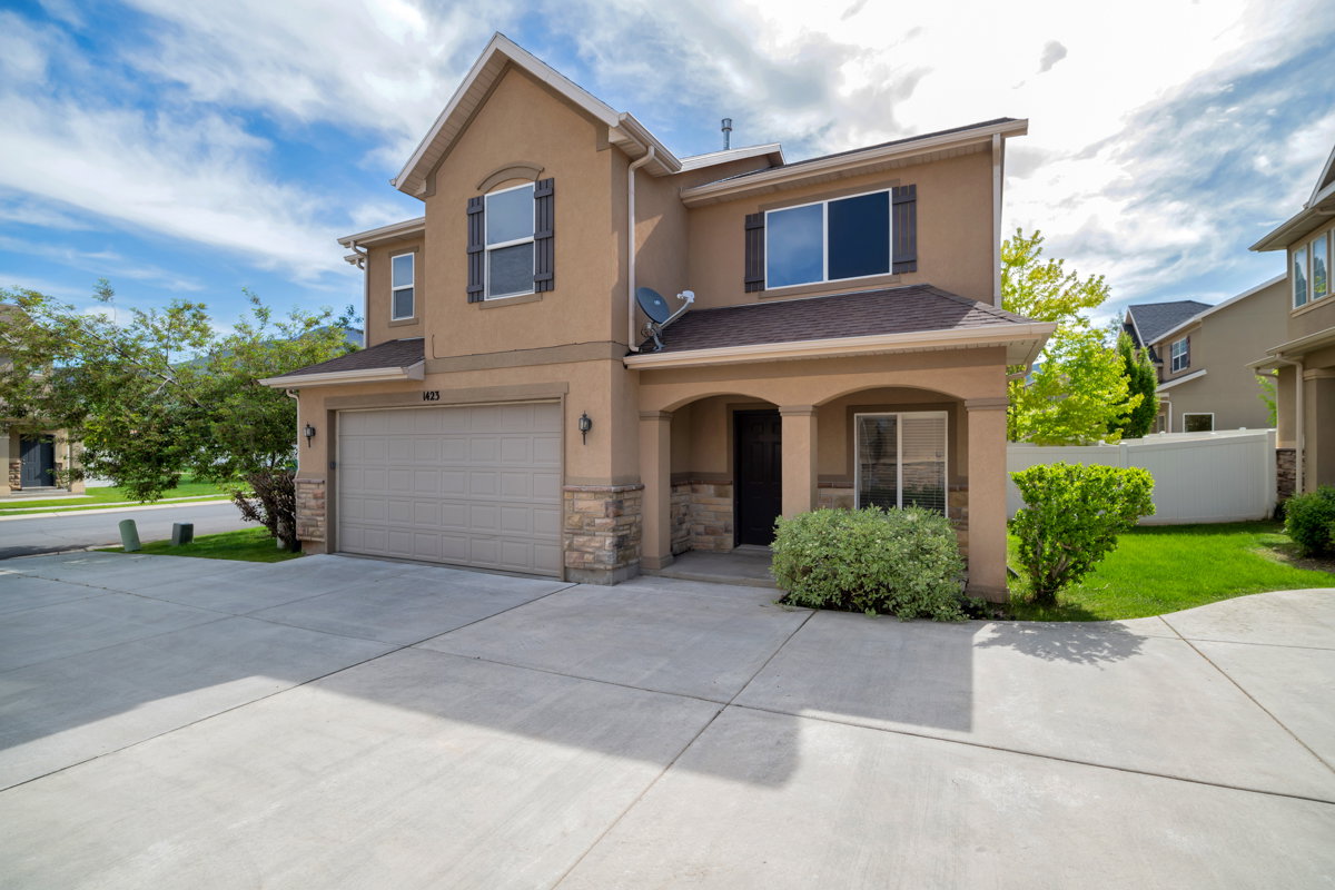 Two-story stucco and stone-faced residence featuring an attached garage, covered entryway, and a concrete driveway