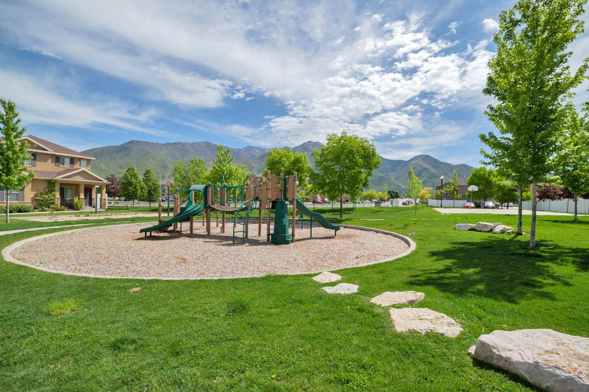 Recreational area featuring a playground with green slides and wood-toned elements, surrounded by a wood chip surface