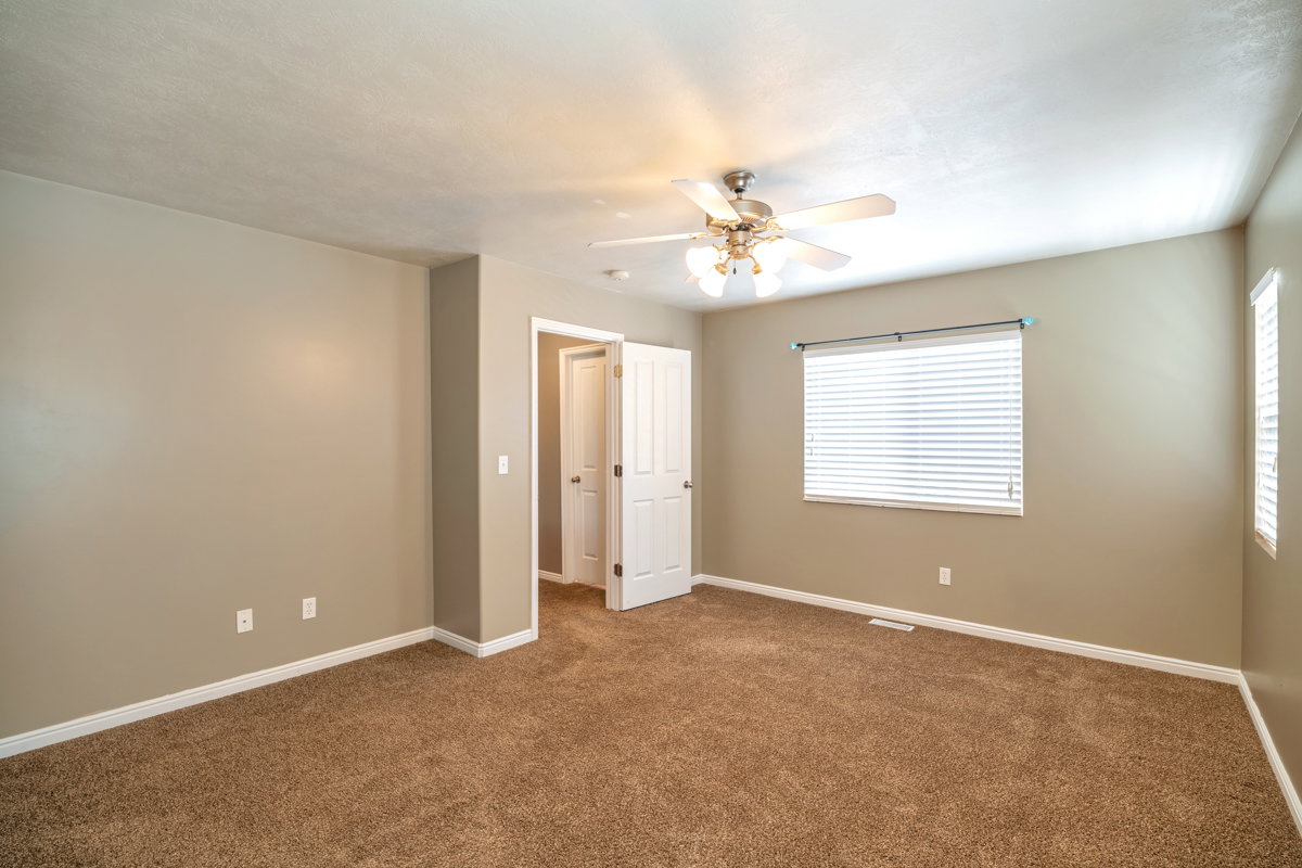Carpeted room featuring a ceiling fan with integrated lighting, a window with horizontal blinds, and a doorway with an open white panel door