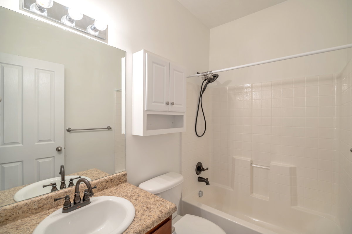 Full bathroom featuring a single vanity with a white oval sink and a mottled countertop, a toilet, a shower-tub combination with white subway-style tile surround, a wall-mounted medicine cabinet with open shelving, and a large mirror with overhead vanity